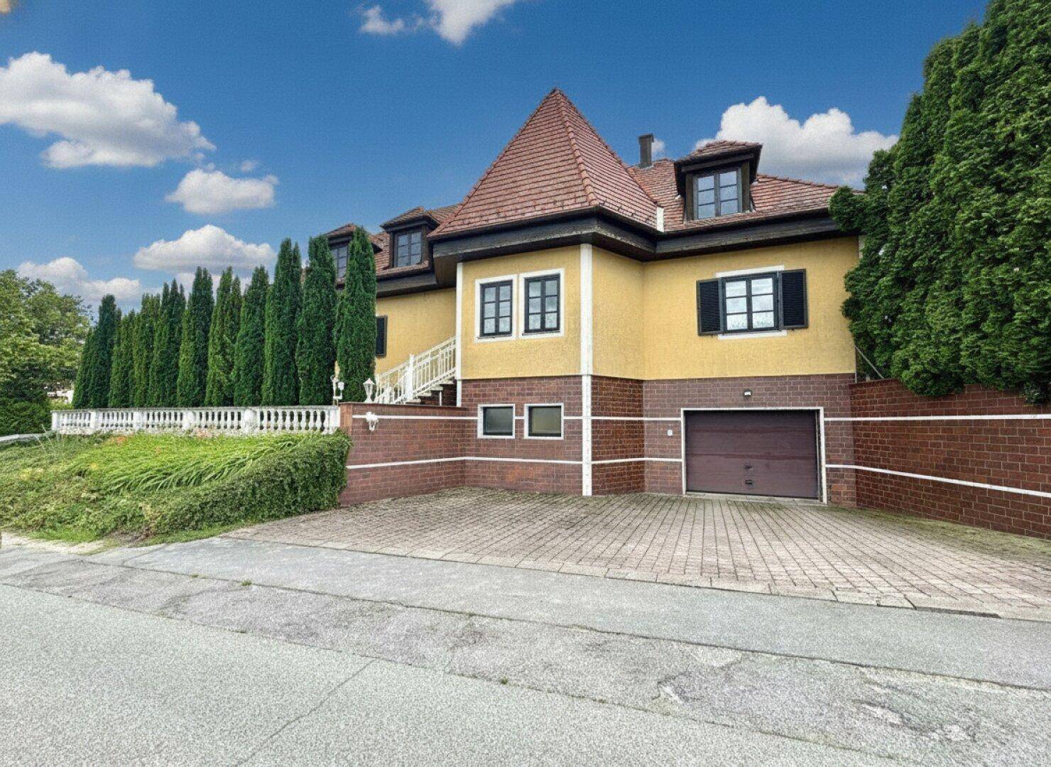 Vorderansicht des Hauses mit Garage, gepflasterter Einfahrt und hohen Hecken.