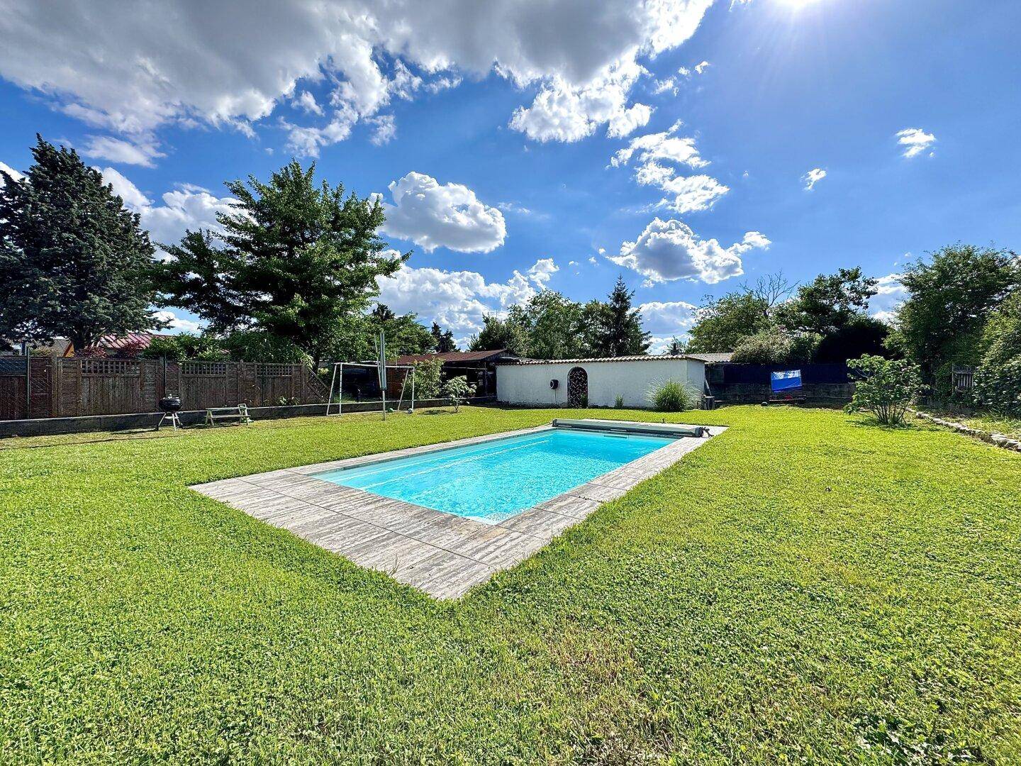 Sonniger Garten mit rechteckigem Pool, umgeben von einer gepflegten Rasenfläche.