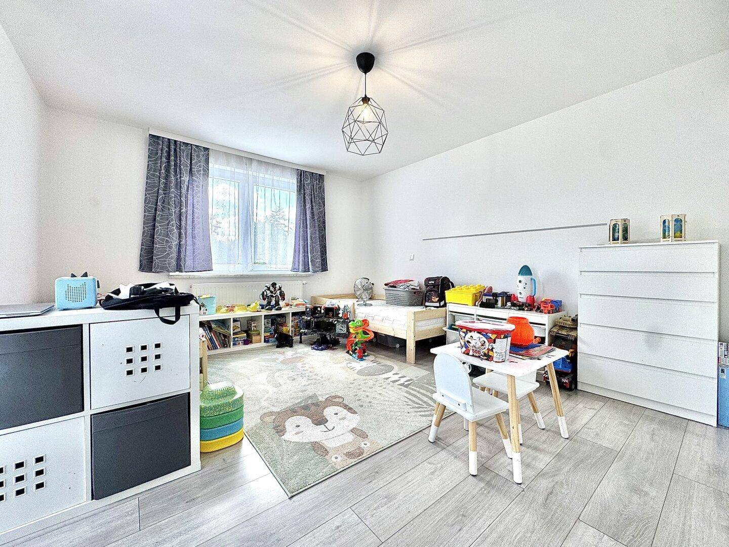 Kinderzimmer mit hellem Boden, Spielzeug und einem großen Fenster für viel Tageslicht.