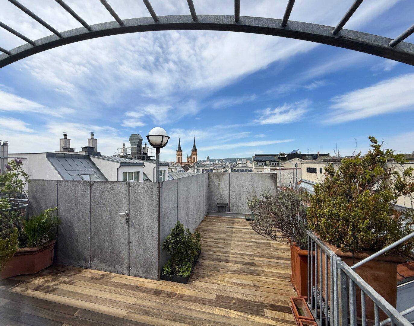 Geräumige Dachterrasse mit Holzboden, Pflanzen und weitem Blick über die Stadt mit Kirchtürmen.