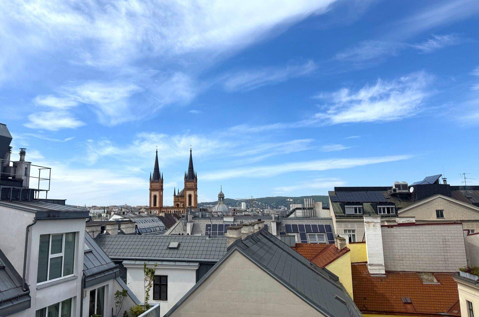 Weitläufiger Blick über die Dächer der Stadt mit historischen Kirchtürmen unter blauem Himmel.