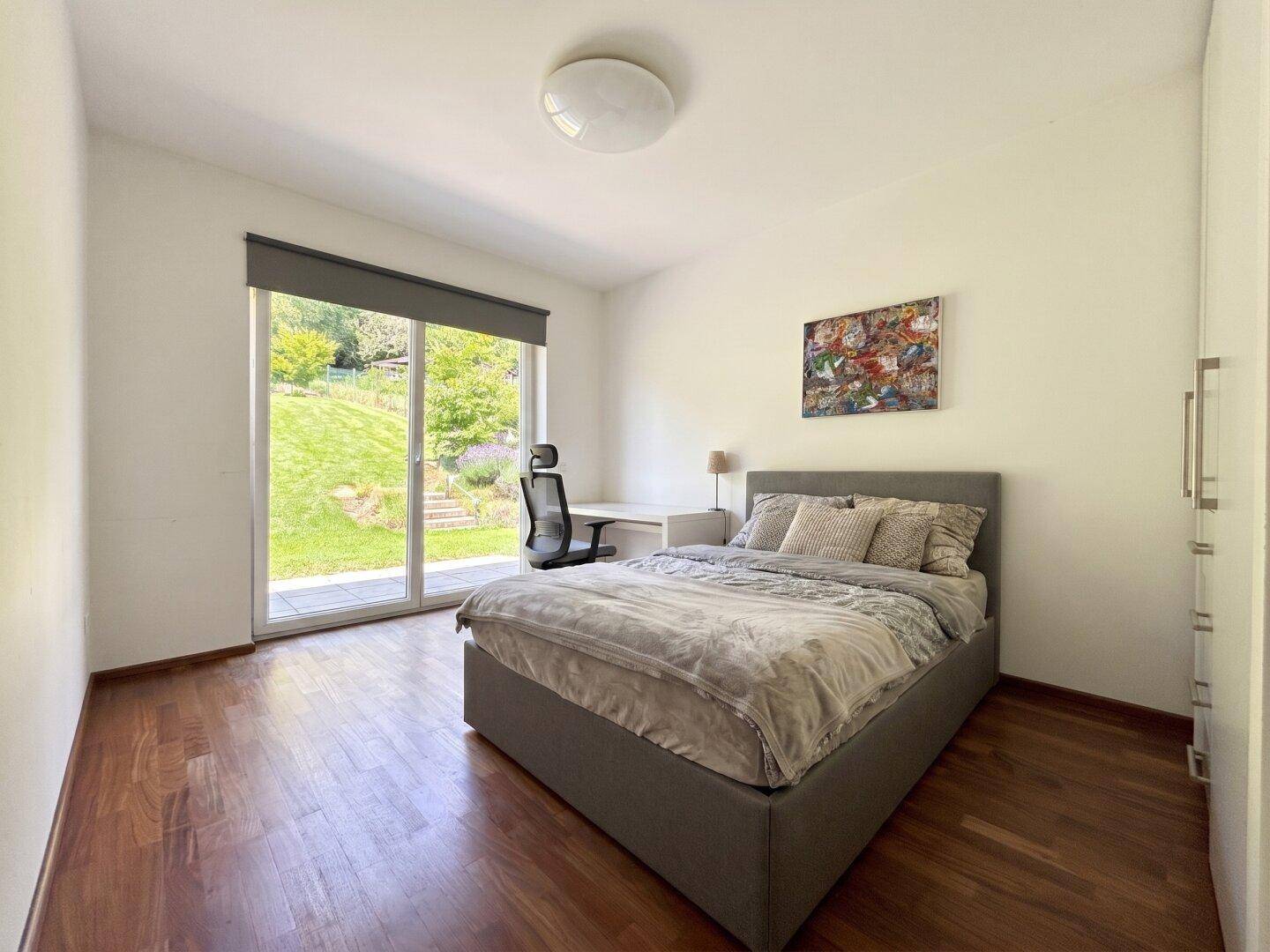 Schlafzimmer mit Bett, Schreibtisch, Holzboden und direktem Zugang zum Garten.