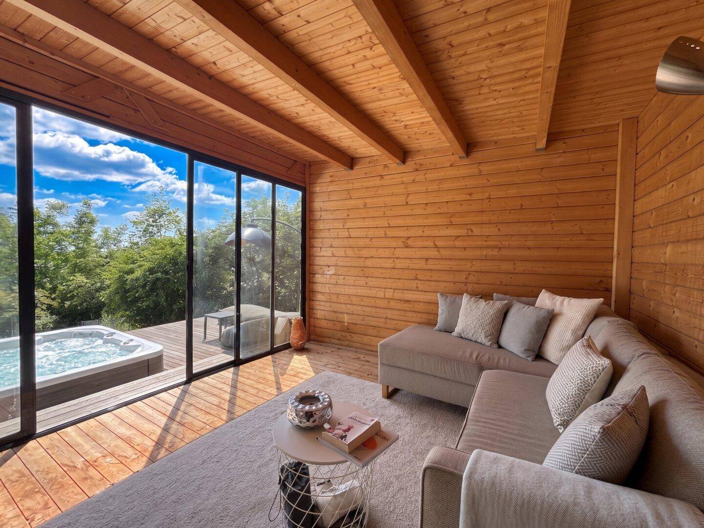 Gemütlicher Innenraum mit Holzwänden, großer Glasfront und Blick auf den Whirlpool im Freien.