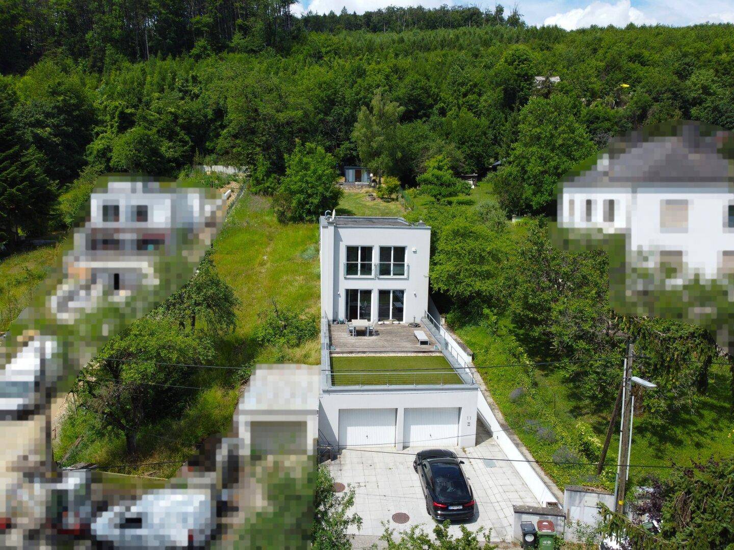 Luftaufnahme eines modernen Hauses mit Flachdach, Garagen und umgebender grüner Hügellandschaft.