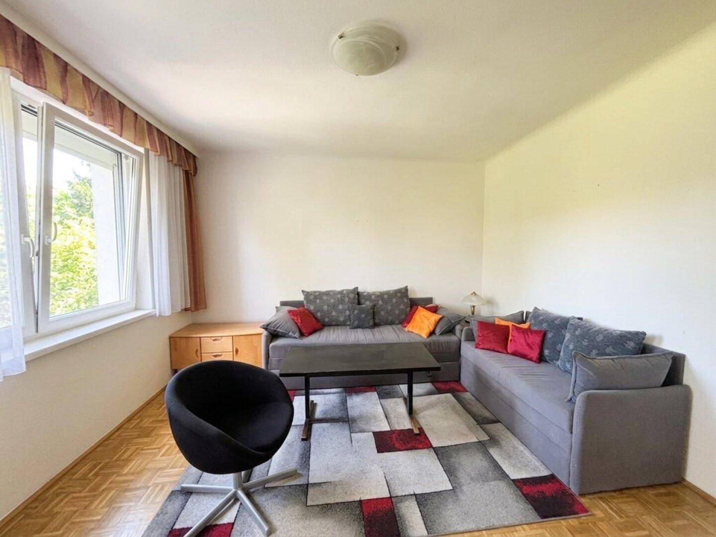 Helles Wohnzimmer mit Parkettboden, zwei Sofas und großem Fenster mit Blick ins Grüne.