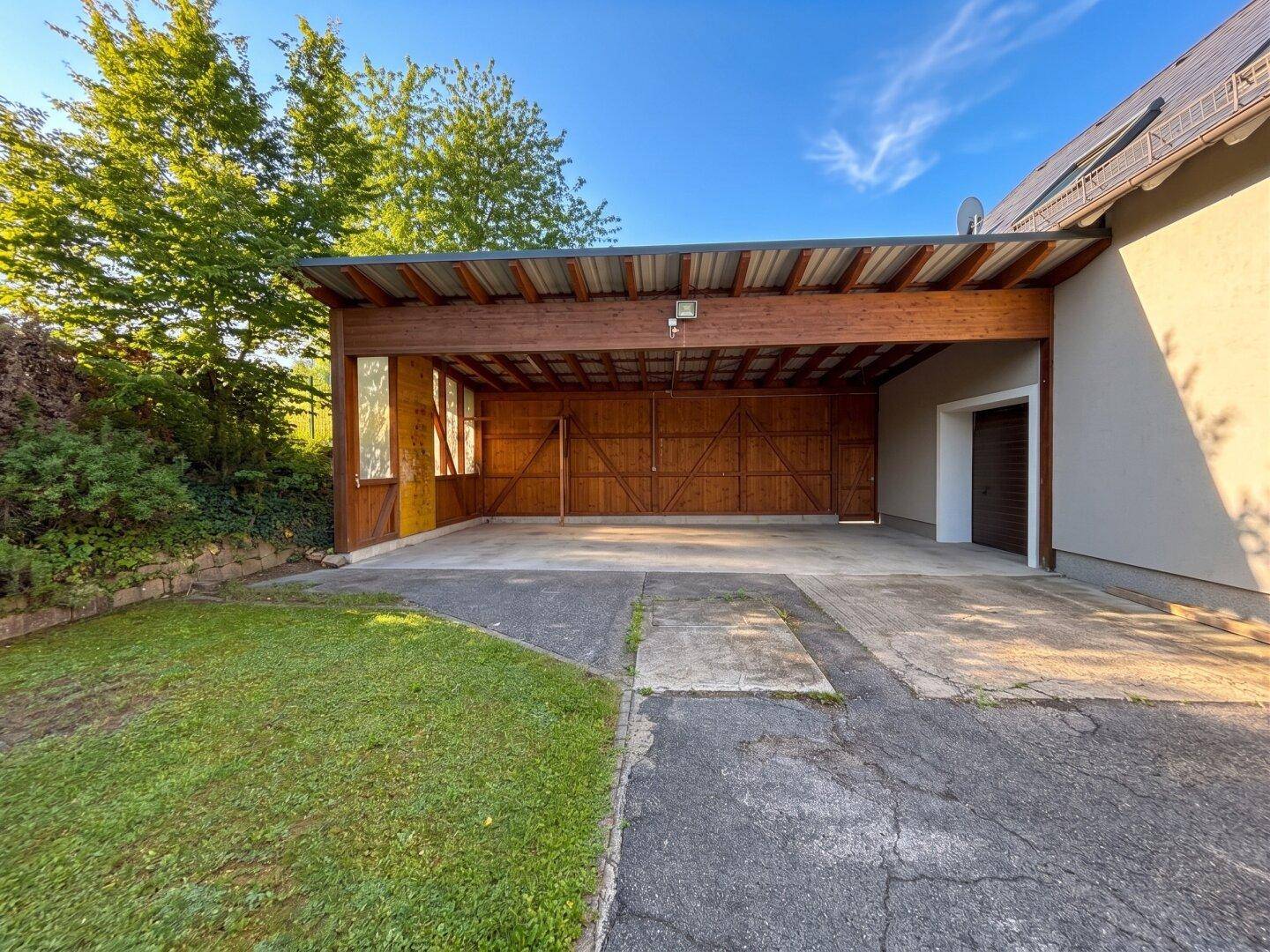 Geräumiger Carport mit Holzkonstruktion und Betonboden, bietet Schutz für mehrere Fahrzeuge.
