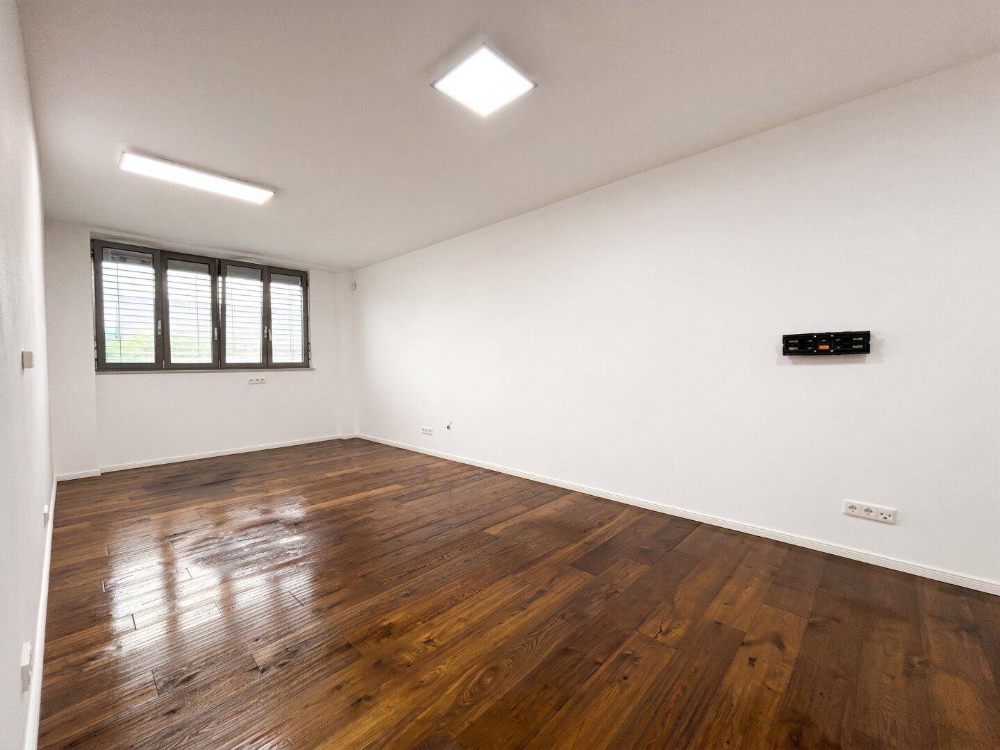 Helles, leeres Zimmer mit dunklem Holzboden und großen Fenstern, bereit zur individuellen Gestaltung.