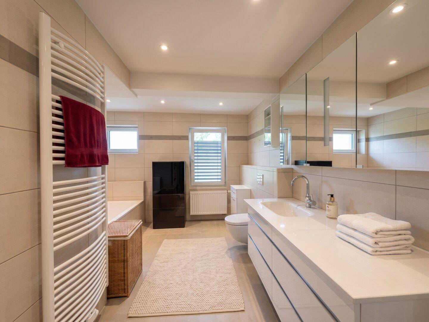 Modernes Badezimmer mit beigen Fliesen, großem Waschtisch, Spiegelschrank und Handtuchheizkörper.