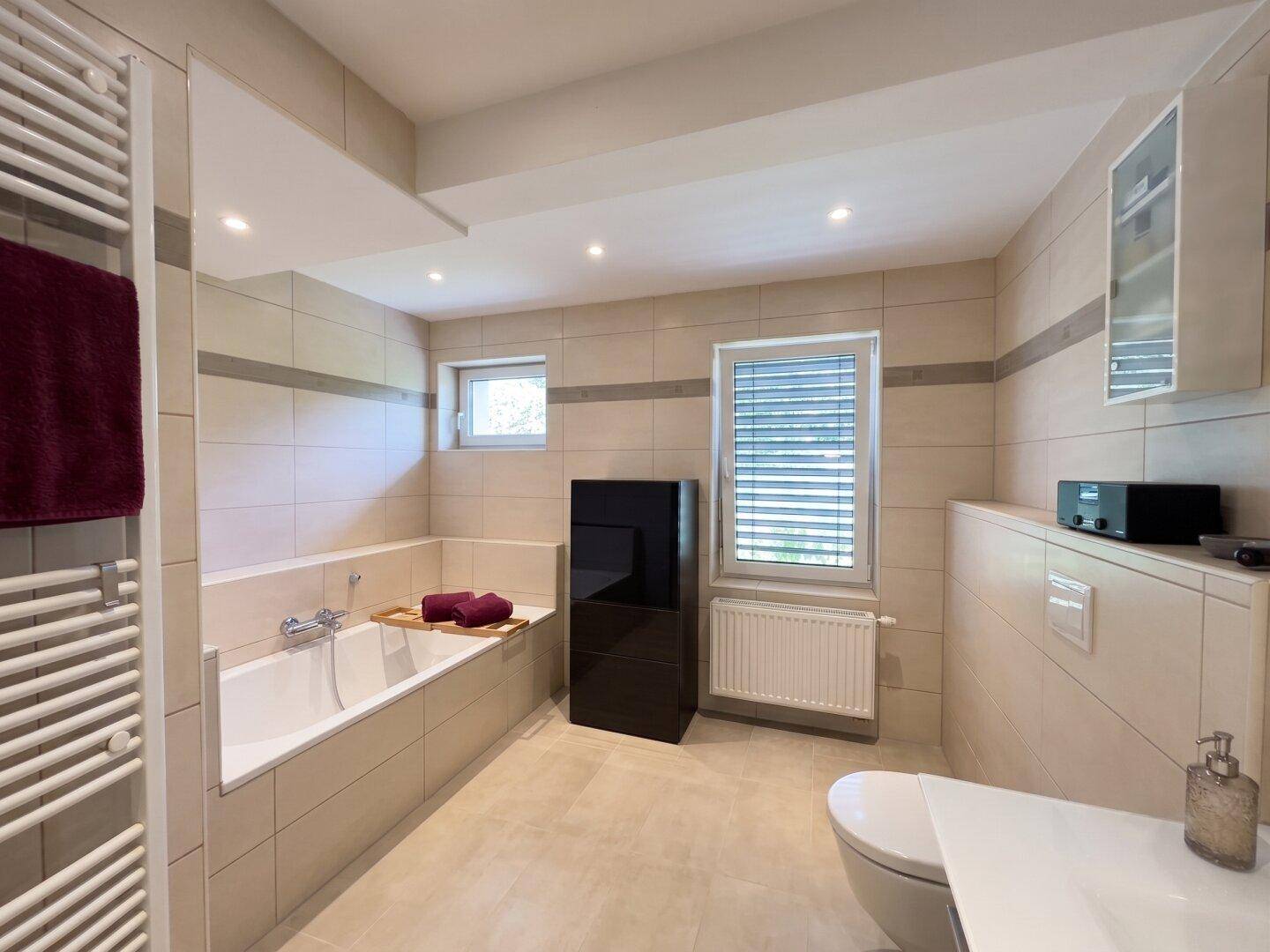 Geräumiges Badezimmer mit eingebauter Badewanne, WC und hellen Fliesen in modernem Design.