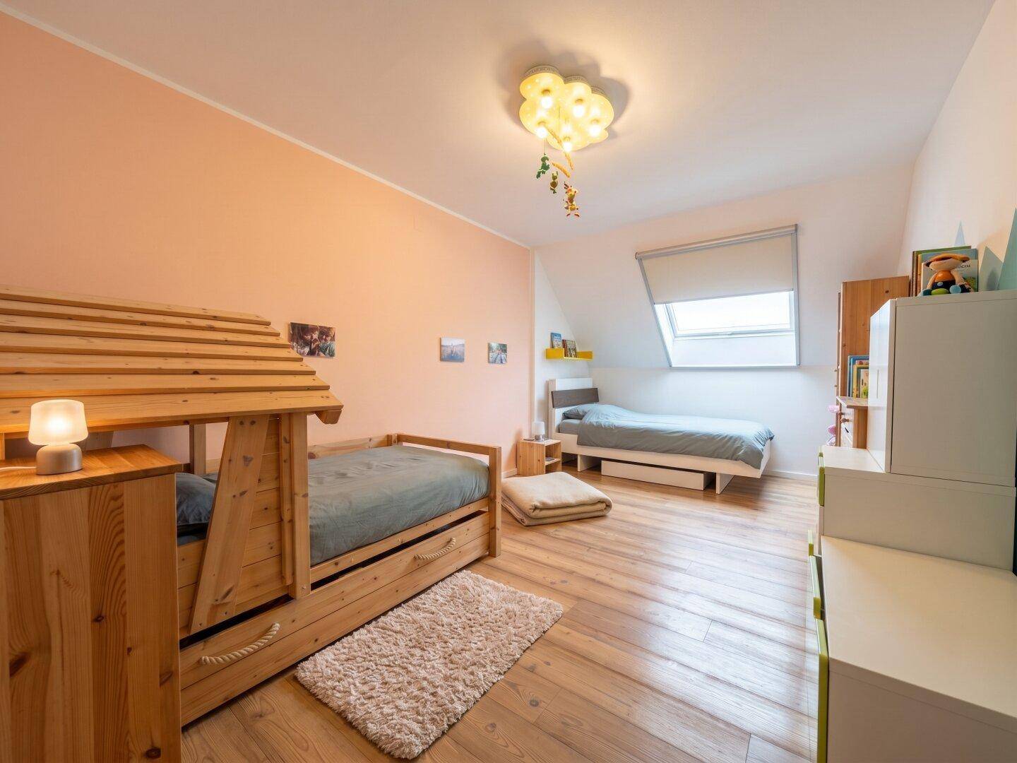 Kinderzimmer mit zwei Betten, Holzboden und einem Dachfenster, das den Raum erhellt.
