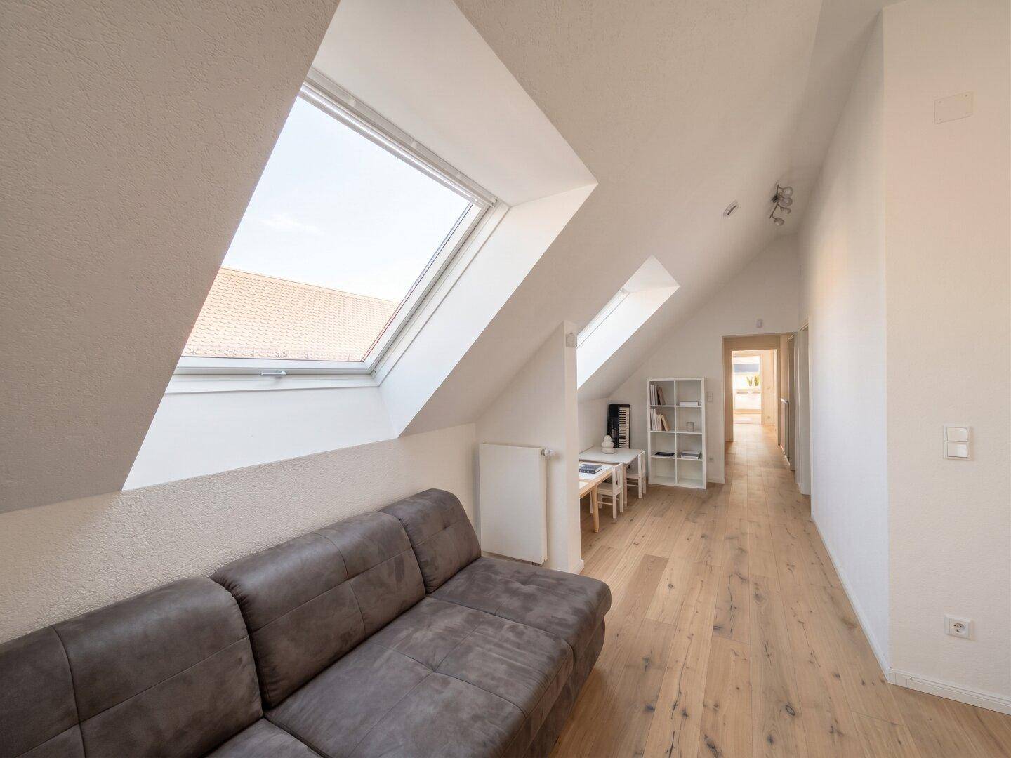Heller Flur im Obergeschoss mit Sofa, Holzboden und mehreren Dachfenstern für viel Tageslicht.