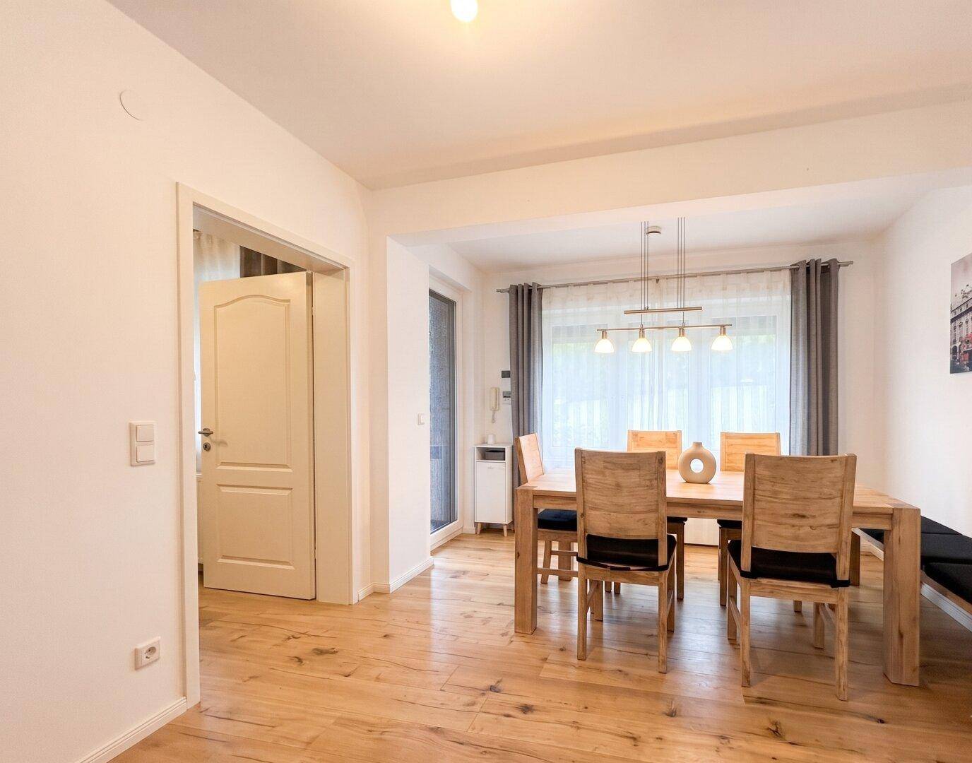 Gemütlicher Essbereich mit Holztisch, passenden Stühlen und Blick ins Grüne durch das Fenster.