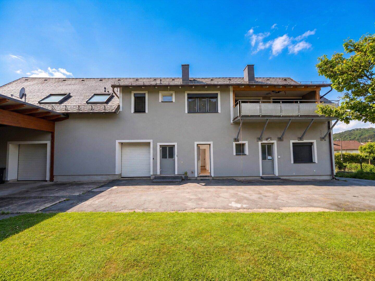 Rückansicht des Hauses mit Balkon, Garagenzugängen und einer gepflegten Rasenfläche.