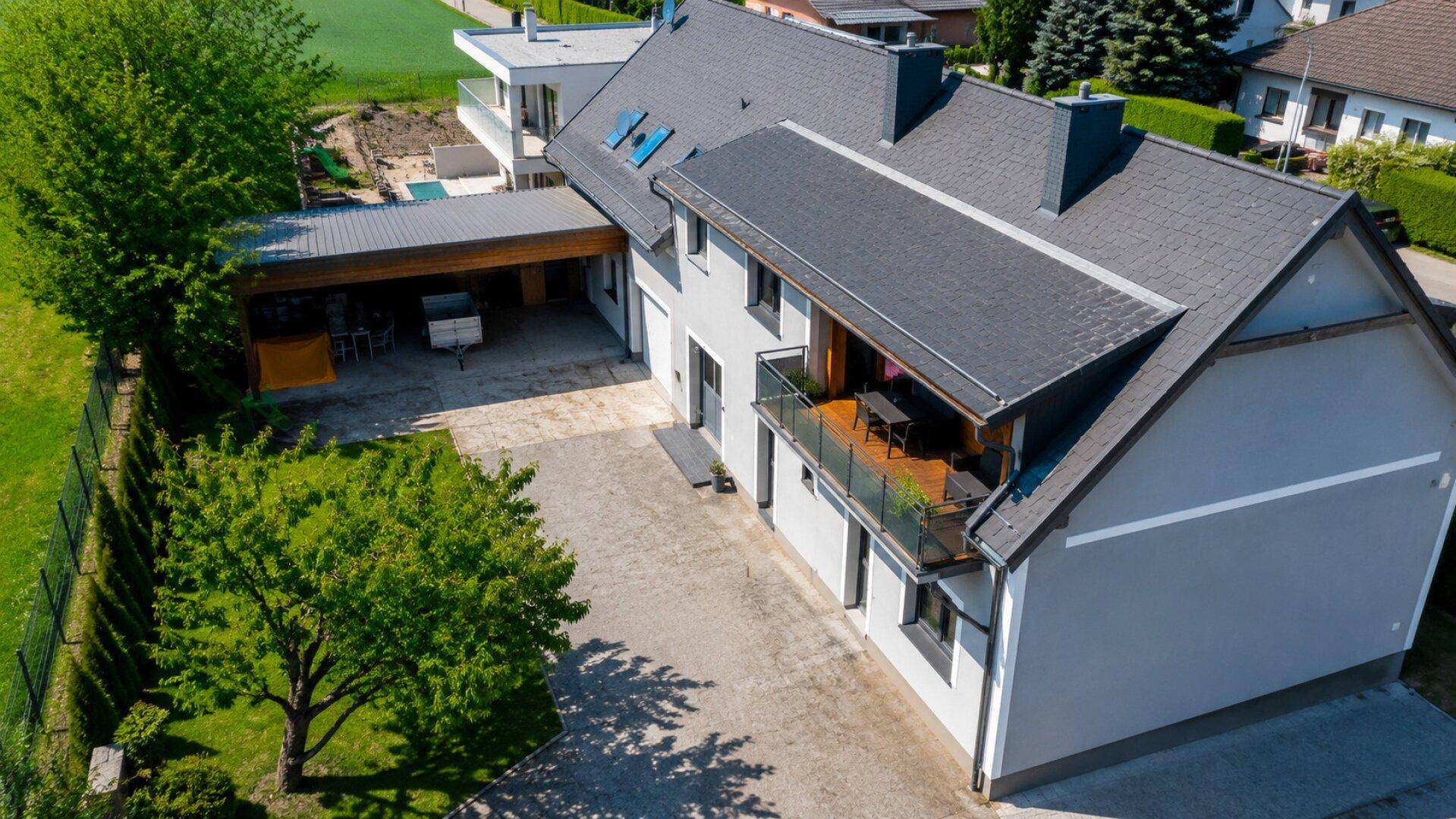 Luftaufnahme des Anwesens mit Haus, Carport, Zufahrt und umliegenden Grünflächen.