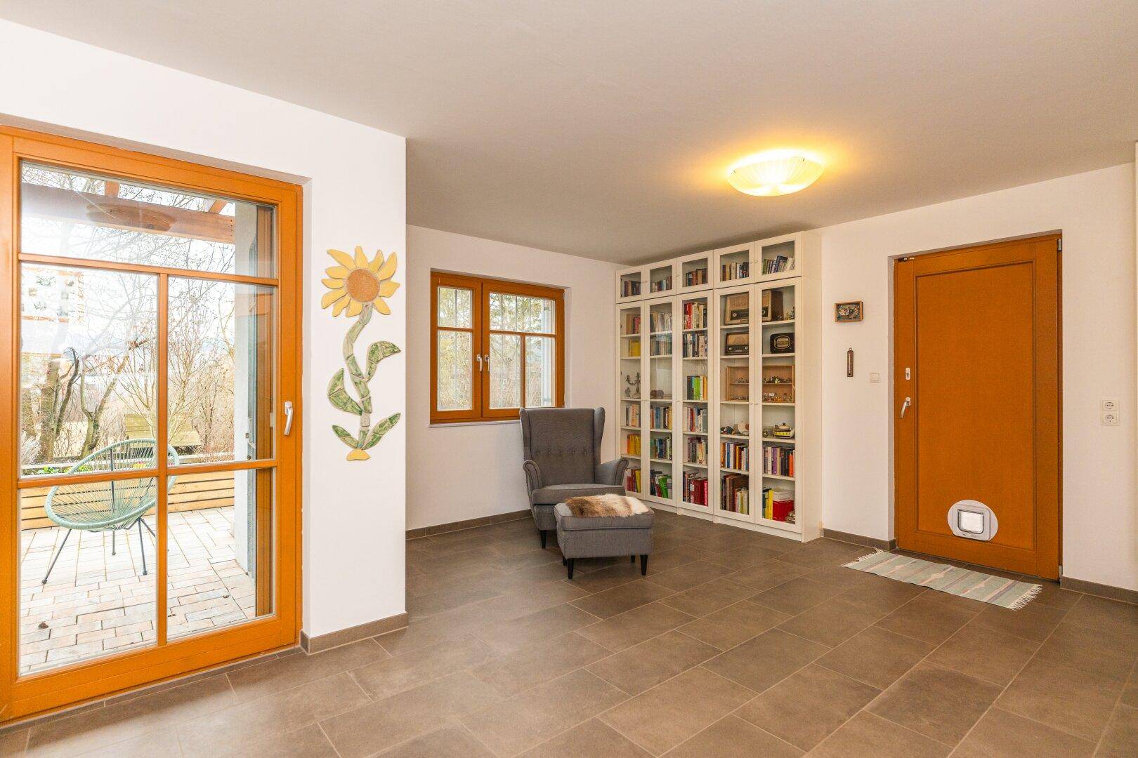 Heller Eingangsbereich mit Bücherregal, Sessel und Zugang zur Terrasse.