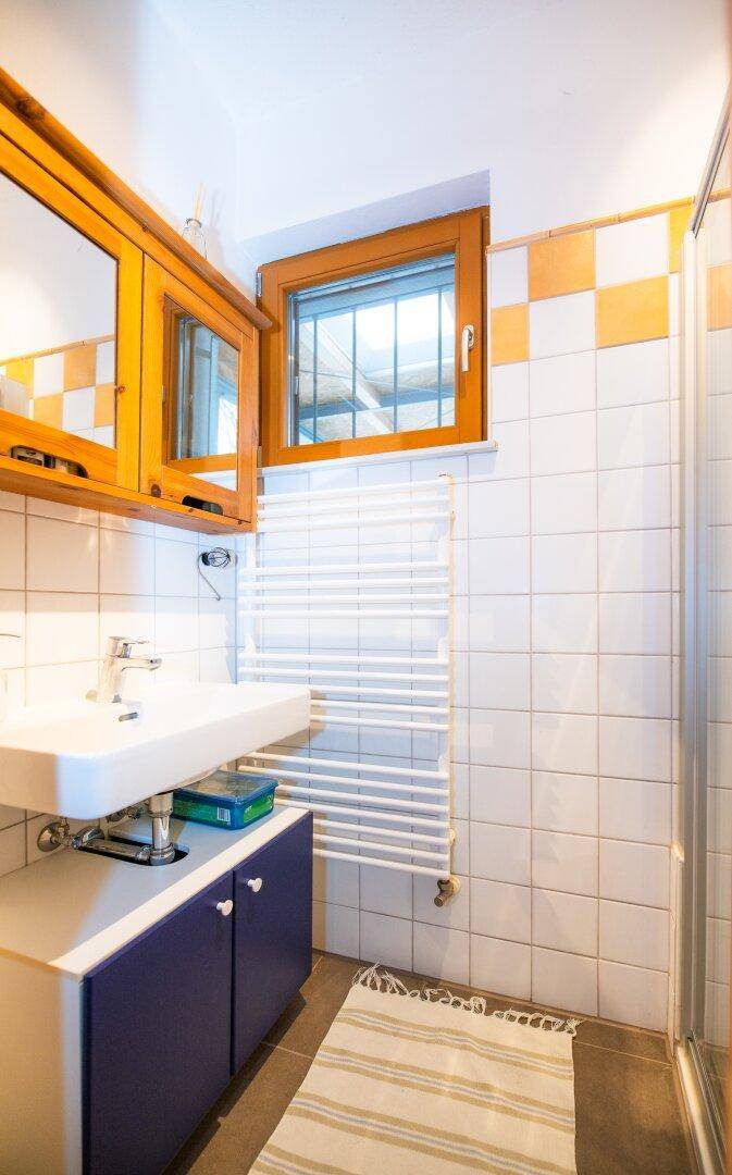 Kleines Badezimmer mit Dusche, Waschbecken, beheiztem Handtuchhalter und Fenster.