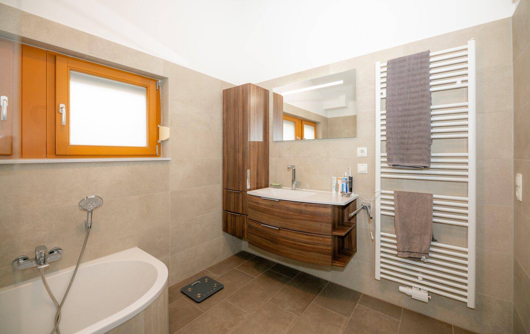 Modernes Badezimmer mit Eckbadewanne, Holzwaschtisch, großem Spiegel und Fenster.