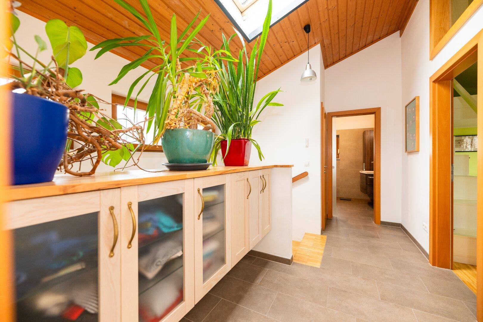 Heller Flur mit Holzdecke, Dachfenster, Einbauschrank und dekorativen Pflanzen.