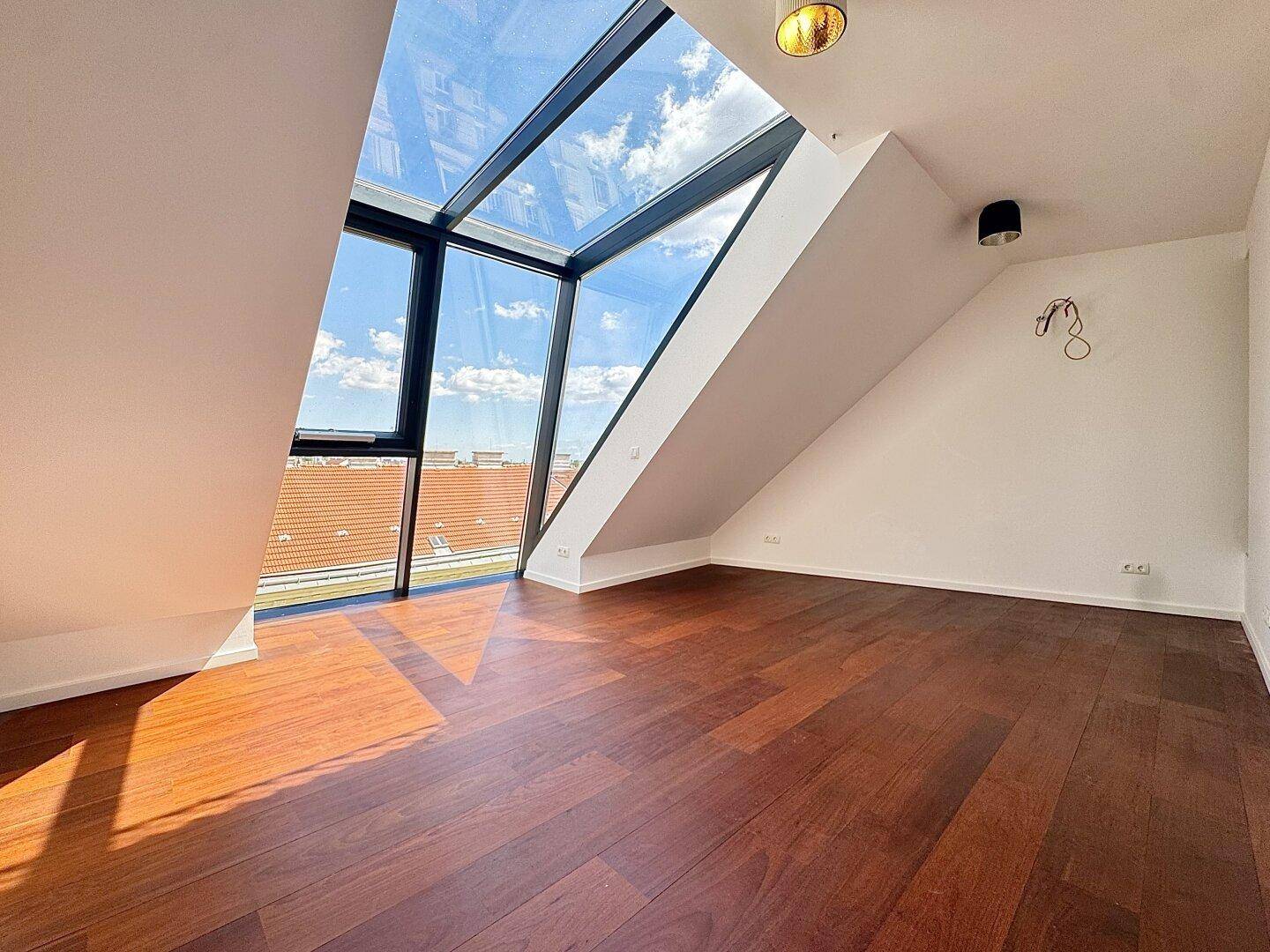 Heller Raum mit dunklem Holzboden und beeindruckender Glasfront, die viel Tageslicht hereinlässt.