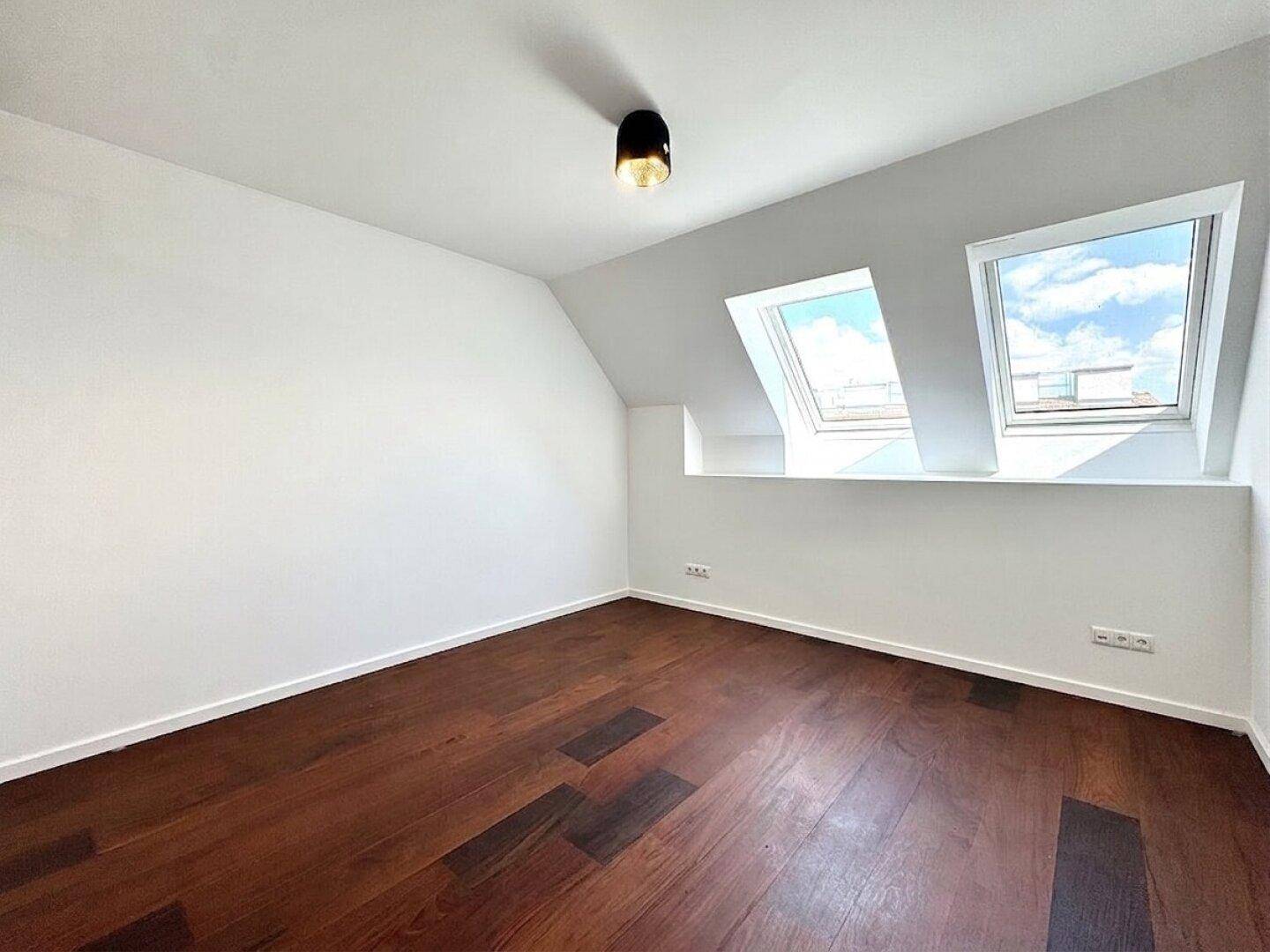 Gemütliches Schlafzimmer im Dachgeschoss mit Holzboden und zwei Dachfenstern für natürliches Licht.