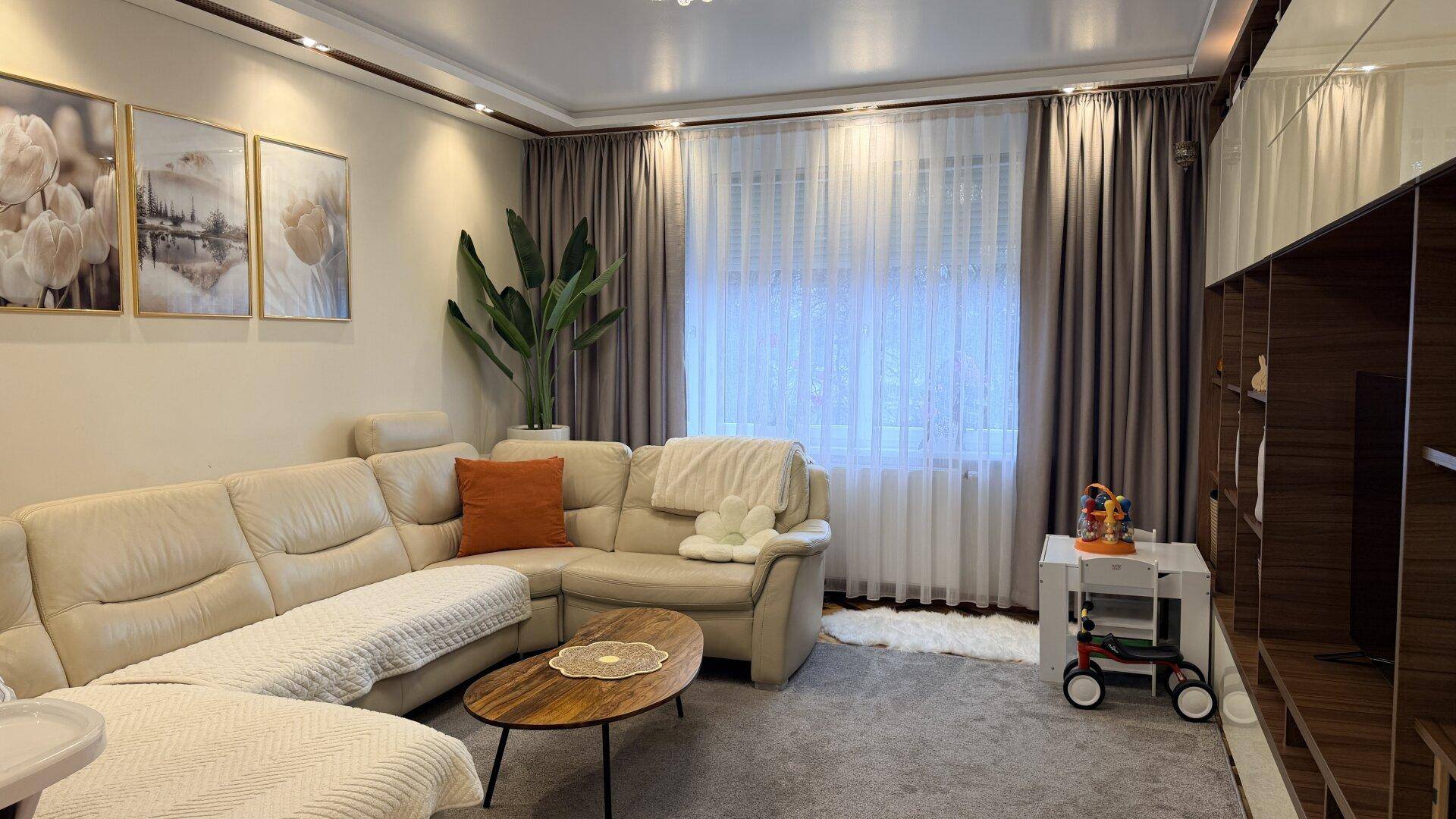 Gemütliches Wohnzimmer mit großem Ecksofa, Teppichboden und dekorativen Bildern an der Wand.