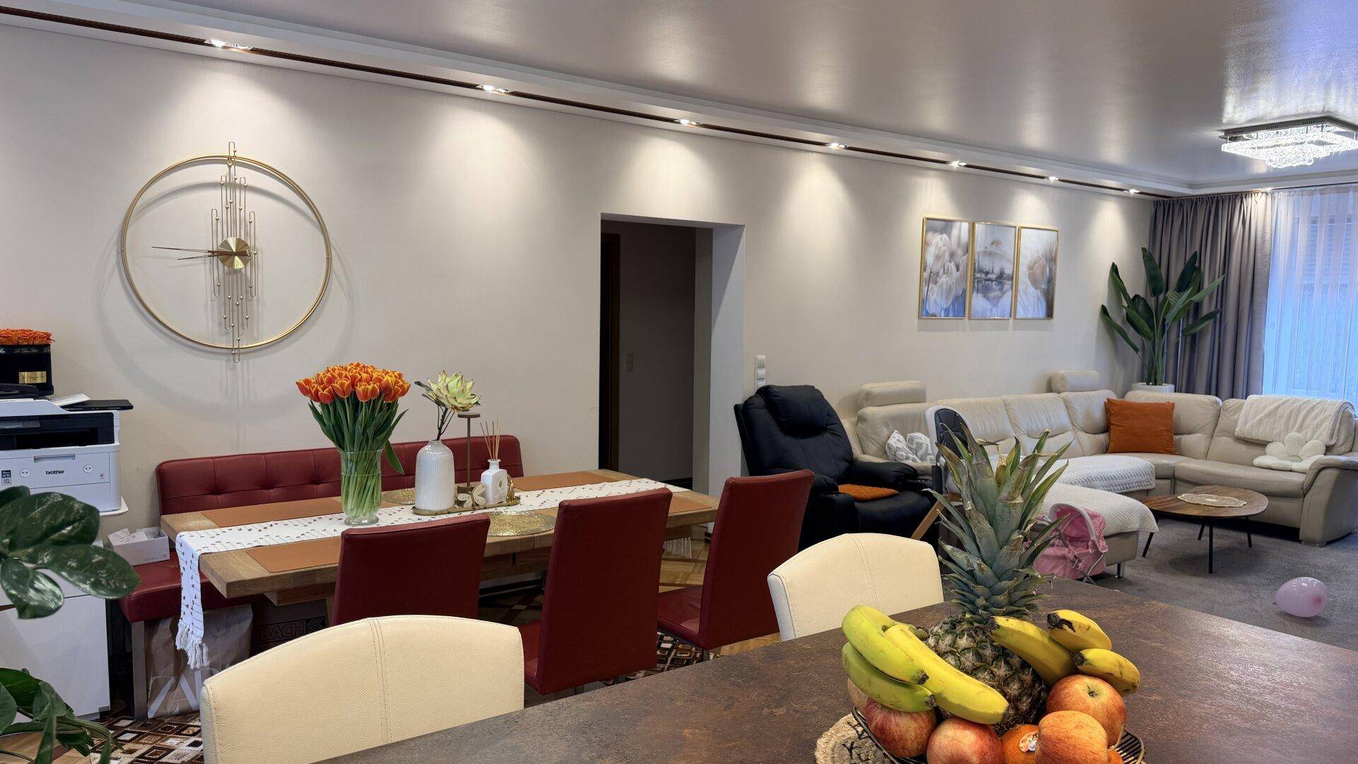 Heller offener Wohn- und Essbereich mit großem Esstisch, bequemen Stühlen und einem Sofa im Hintergrund.