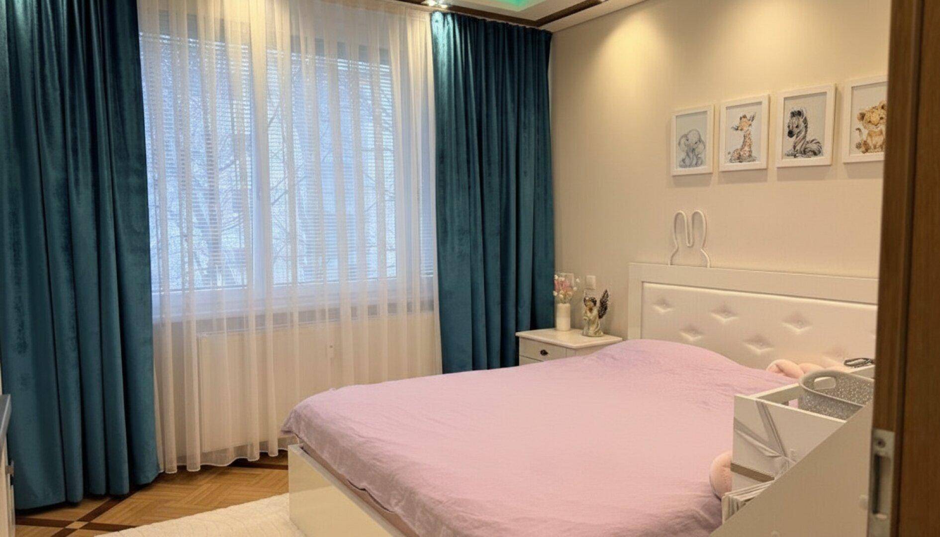 Kinderzimmer mit einem Bett, Holzboden, bunten Vorhängen und Bildern an der Wand.
