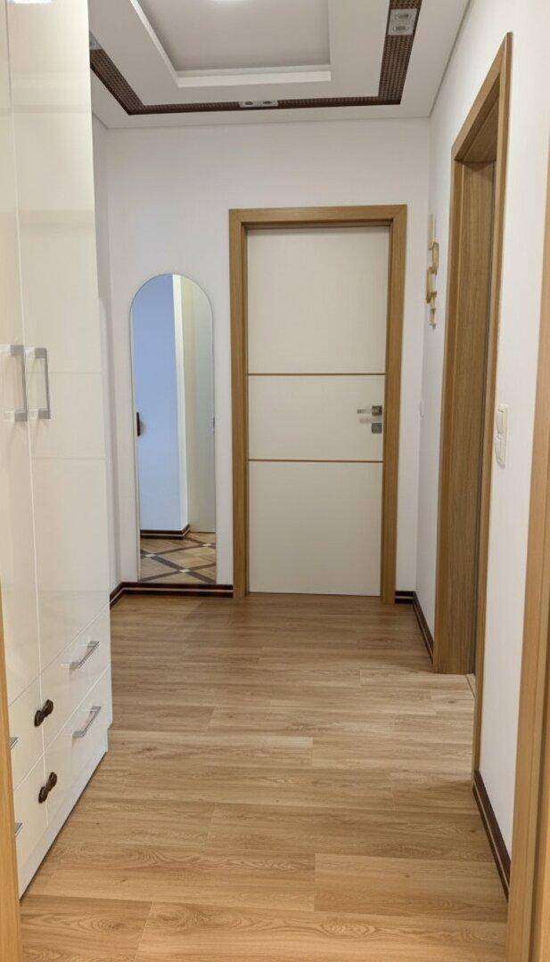 Heller Flur mit Holzboden, modernen Türen und einem Spiegel, der den Raum optisch vergrößert.
