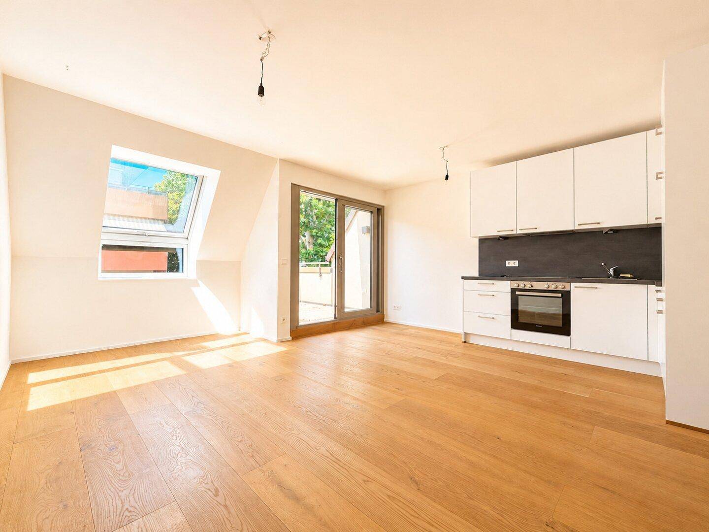 Heller offener Wohnbereich mit Holzboden, Dachfenster und Zugang zu einem Balkon.