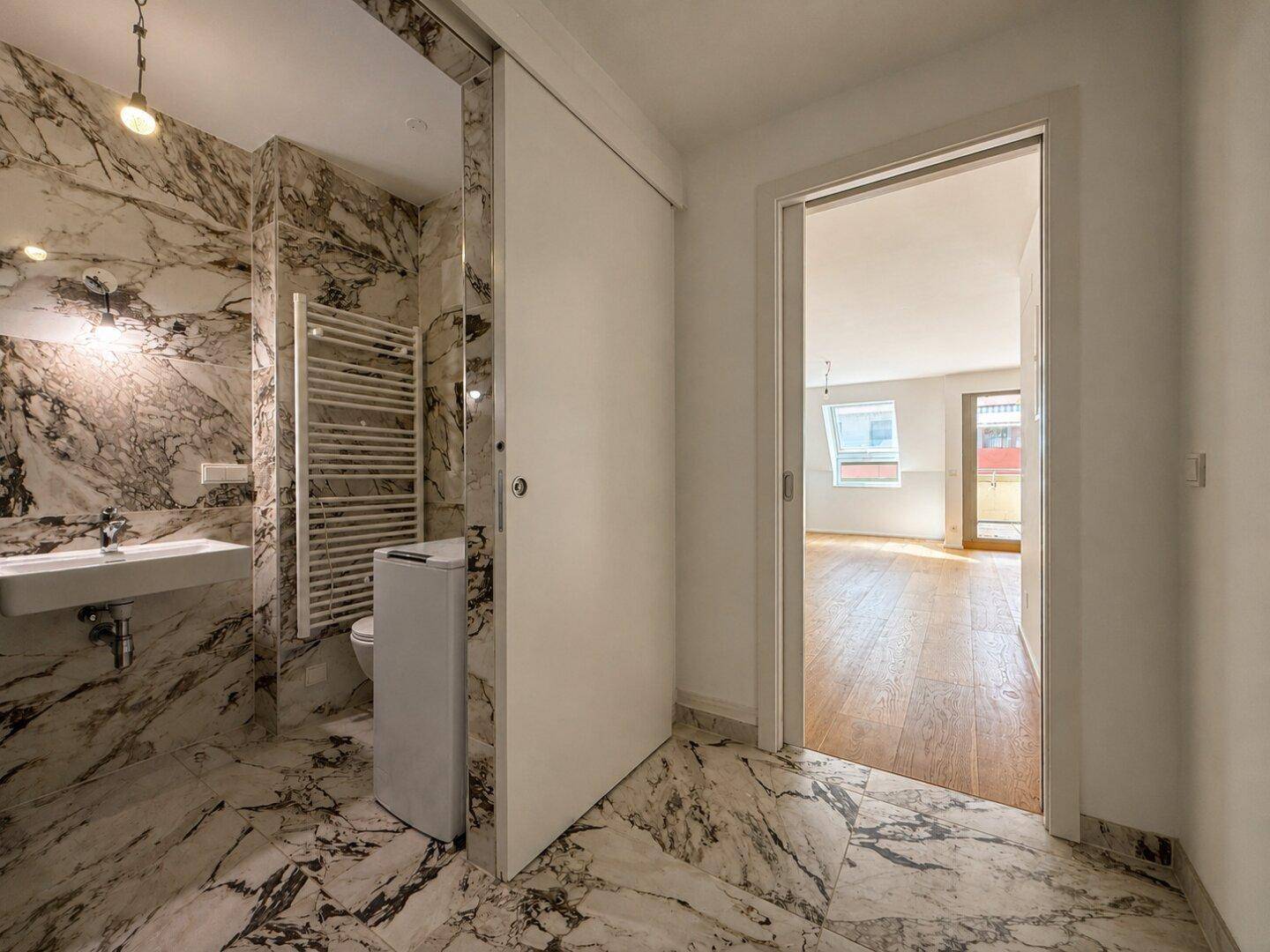 Elegantes Badezimmer mit Marmorfliesen, modernem Waschbecken und Zugang zum Wohnbereich.