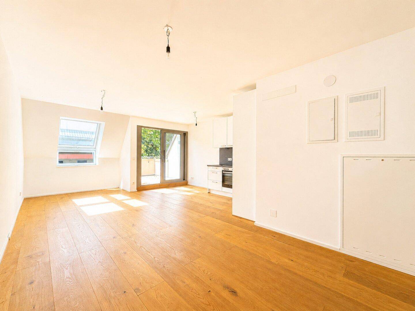 Lichtdurchfluteter Wohnbereich mit Holzboden, Dachfenster und Balkonzugang.