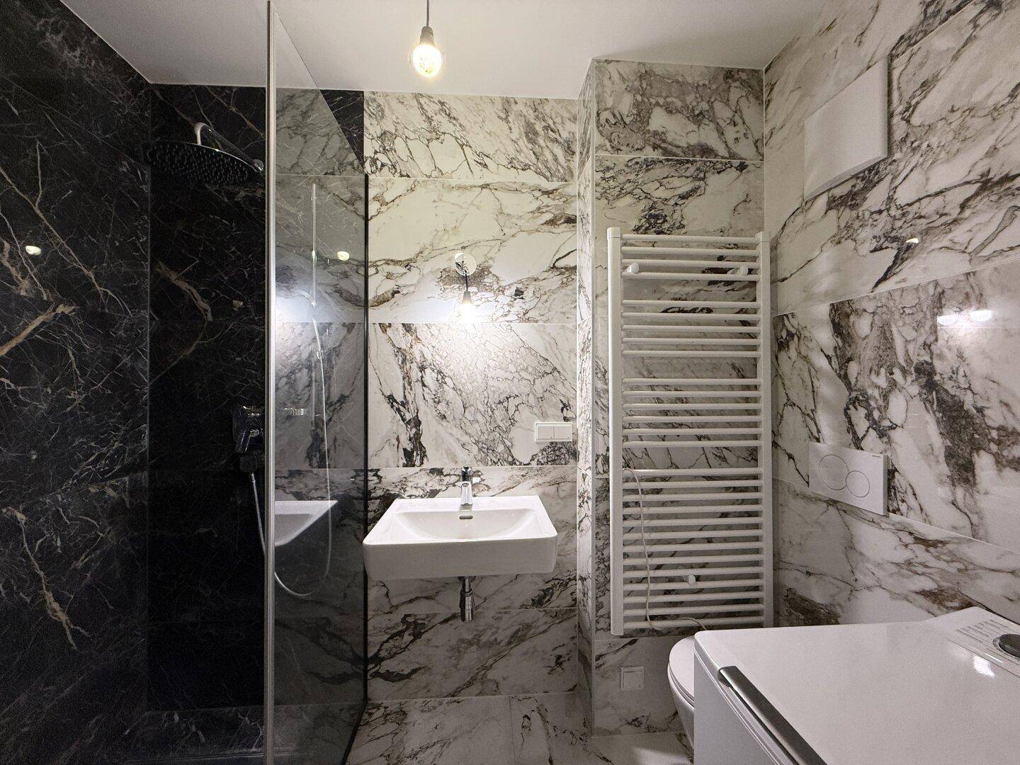 Modernes Badezimmer mit Marmorfliesen, begehbarer Dusche und beheiztem Handtuchhalter.