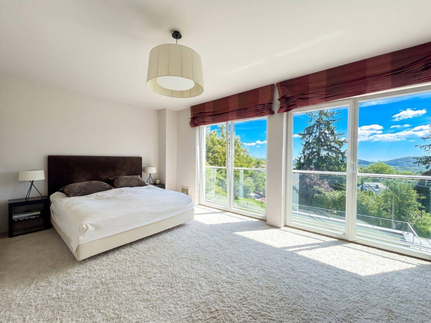 Helles Schlafzimmer mit großem Bett, Teppichboden und raumhohen Fenstern mit weitem Ausblick.