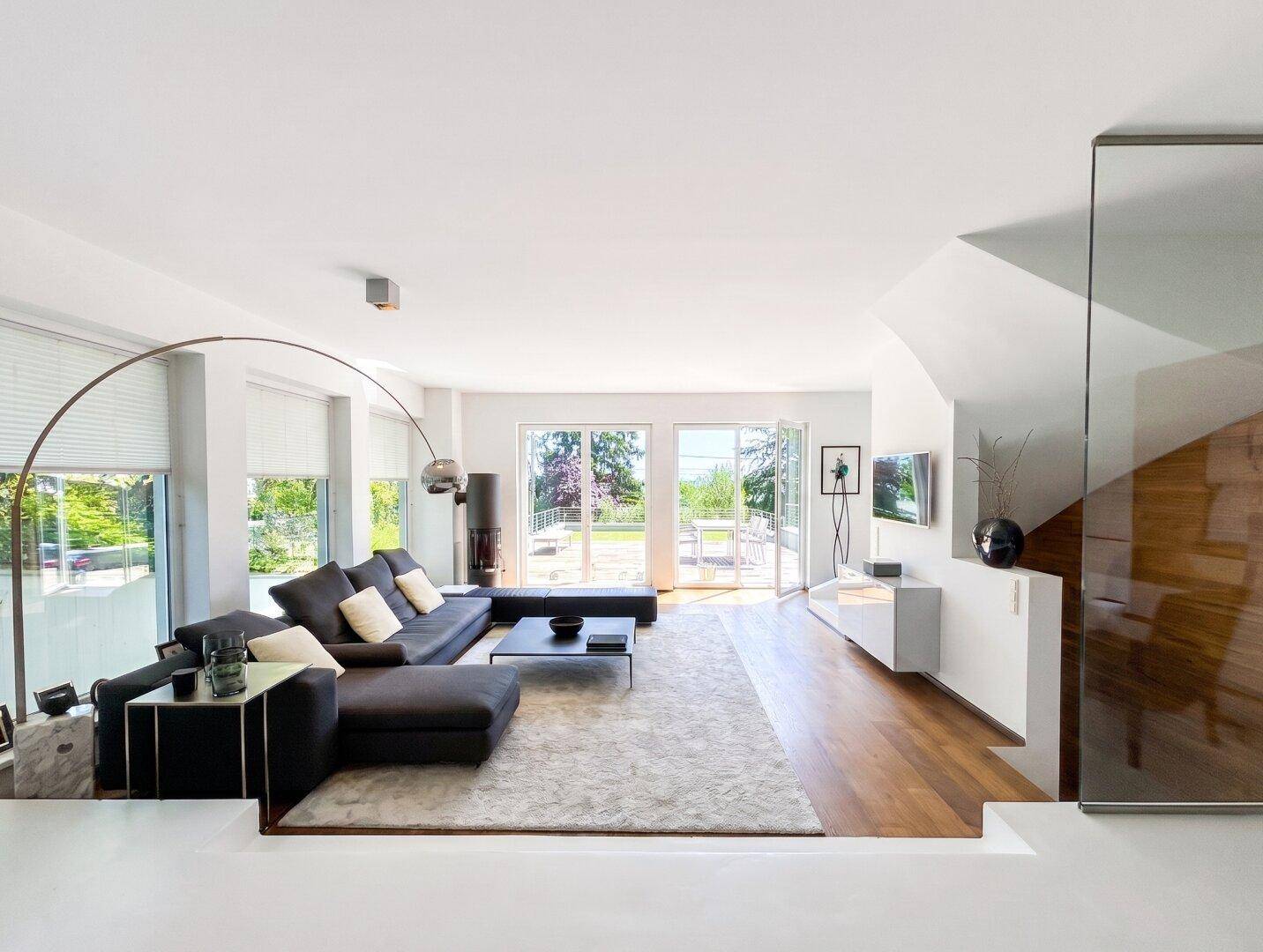 Helles, modernes Wohnzimmer mit großem Sofa, Holzboden und Zugang zu einer Außenterrasse.