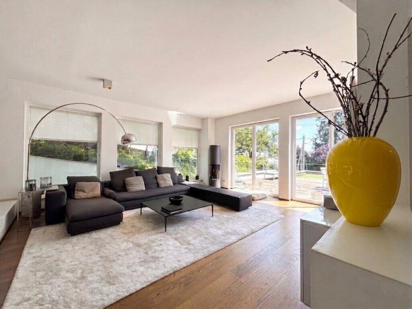 Geräumiges Wohnzimmer mit dunklem Sofa, Holzboden und einem modernen Kamin, hell durch große Fenster.