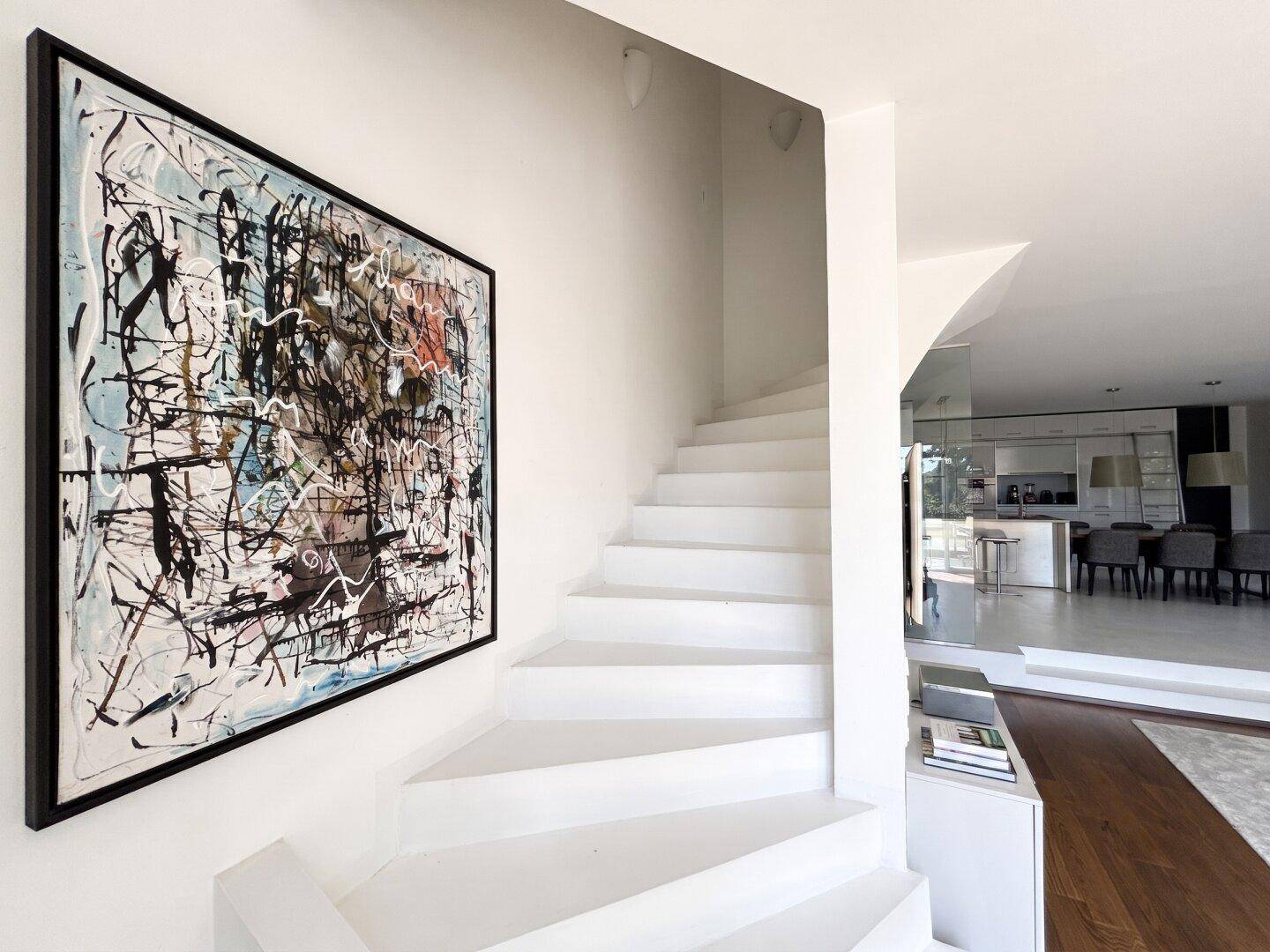 Heller Treppenaufgang mit modernem Kunstwerk, der die verschiedenen Ebenen des Hauses verbindet.