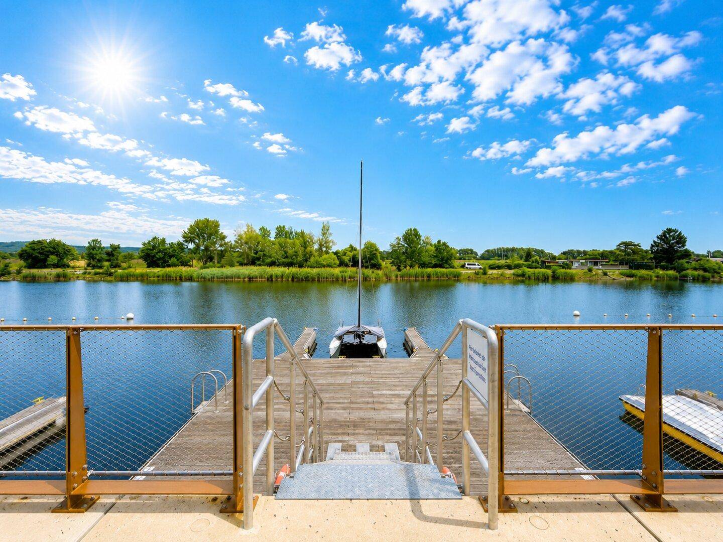Steg mit Bootsanlegestellen und Blick auf den ruhigen See unter strahlend blauem Himmel.