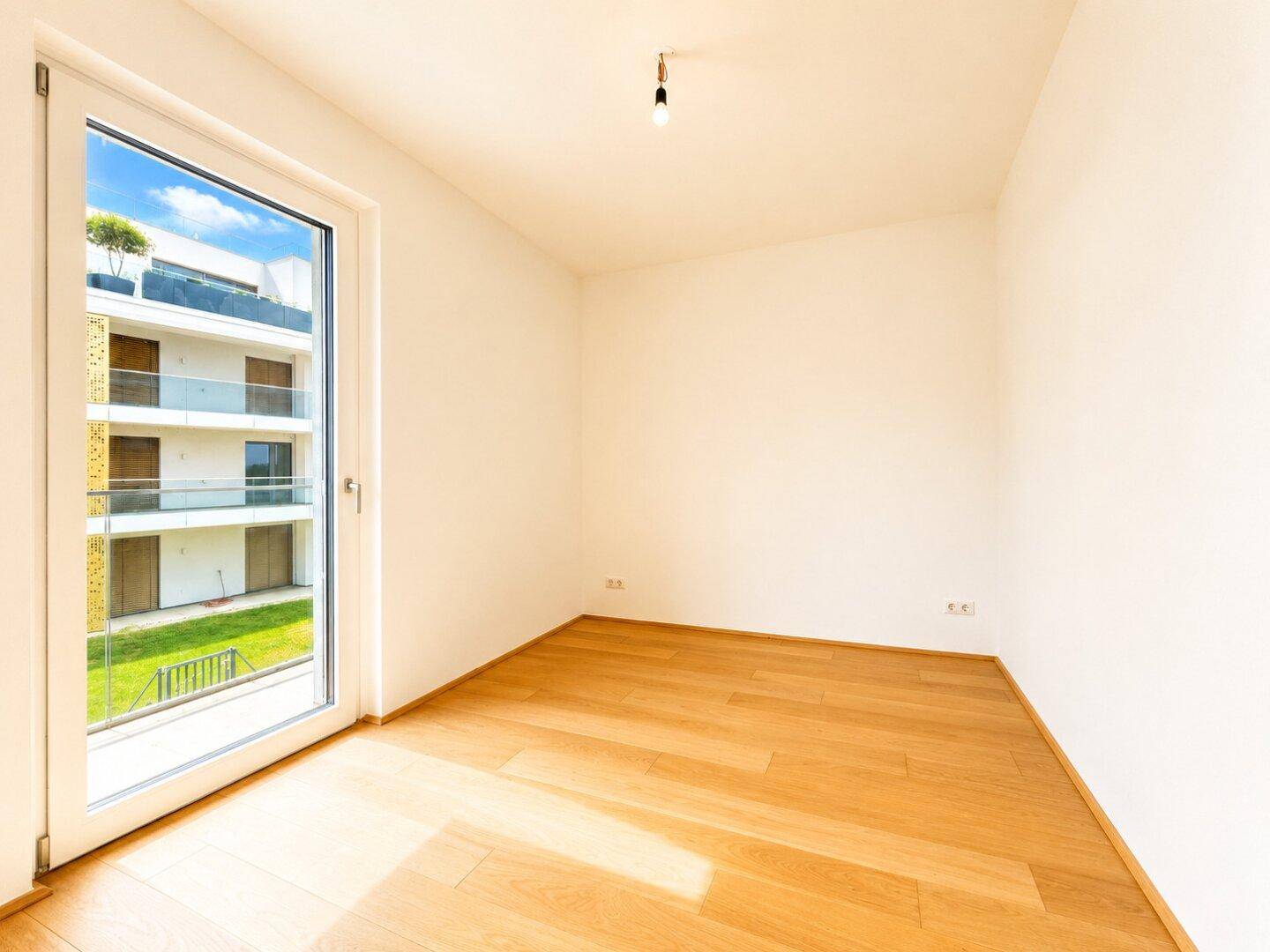 Helles Zimmer mit Holzboden und großer Fensterfront, die viel Tageslicht hereinlässt.