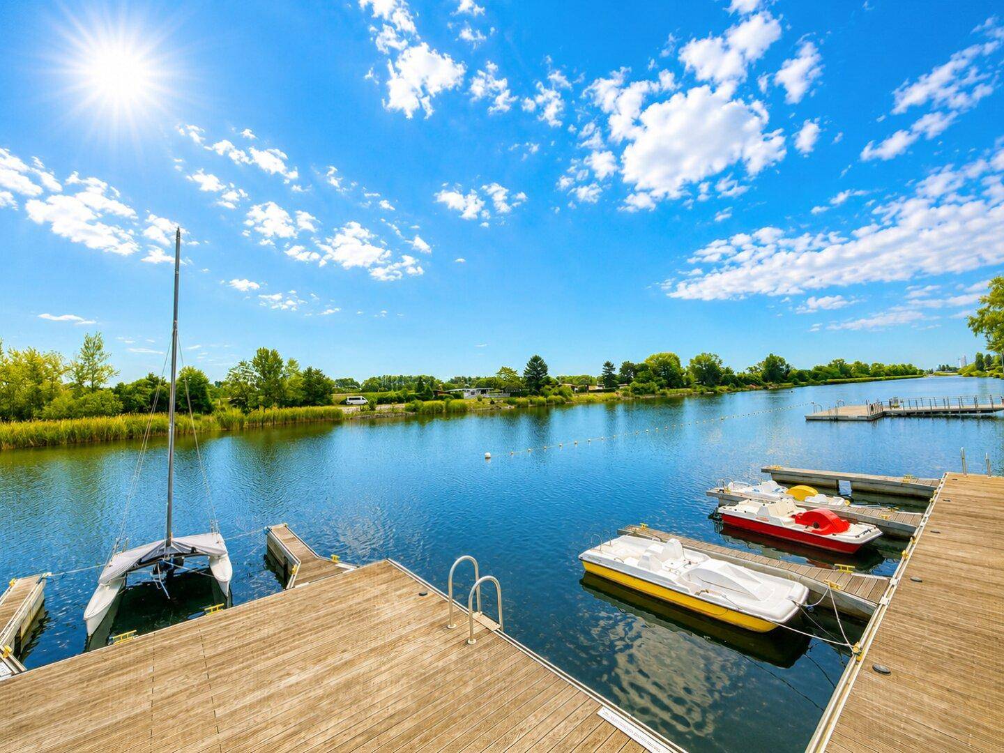 Mehrere Boote an den Anlegestellen am Seeufer unter strahlend blauem Himmel.