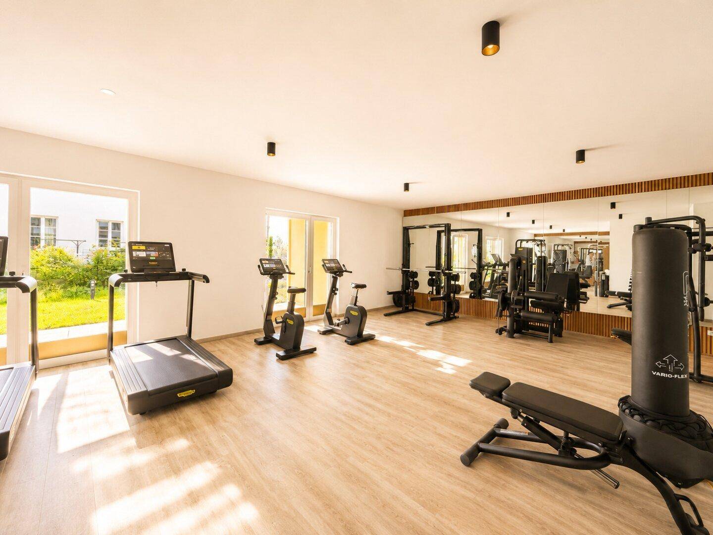 Gut ausgestatteter Fitnessraum mit verschiedenen Geräten und großen Fenstern.