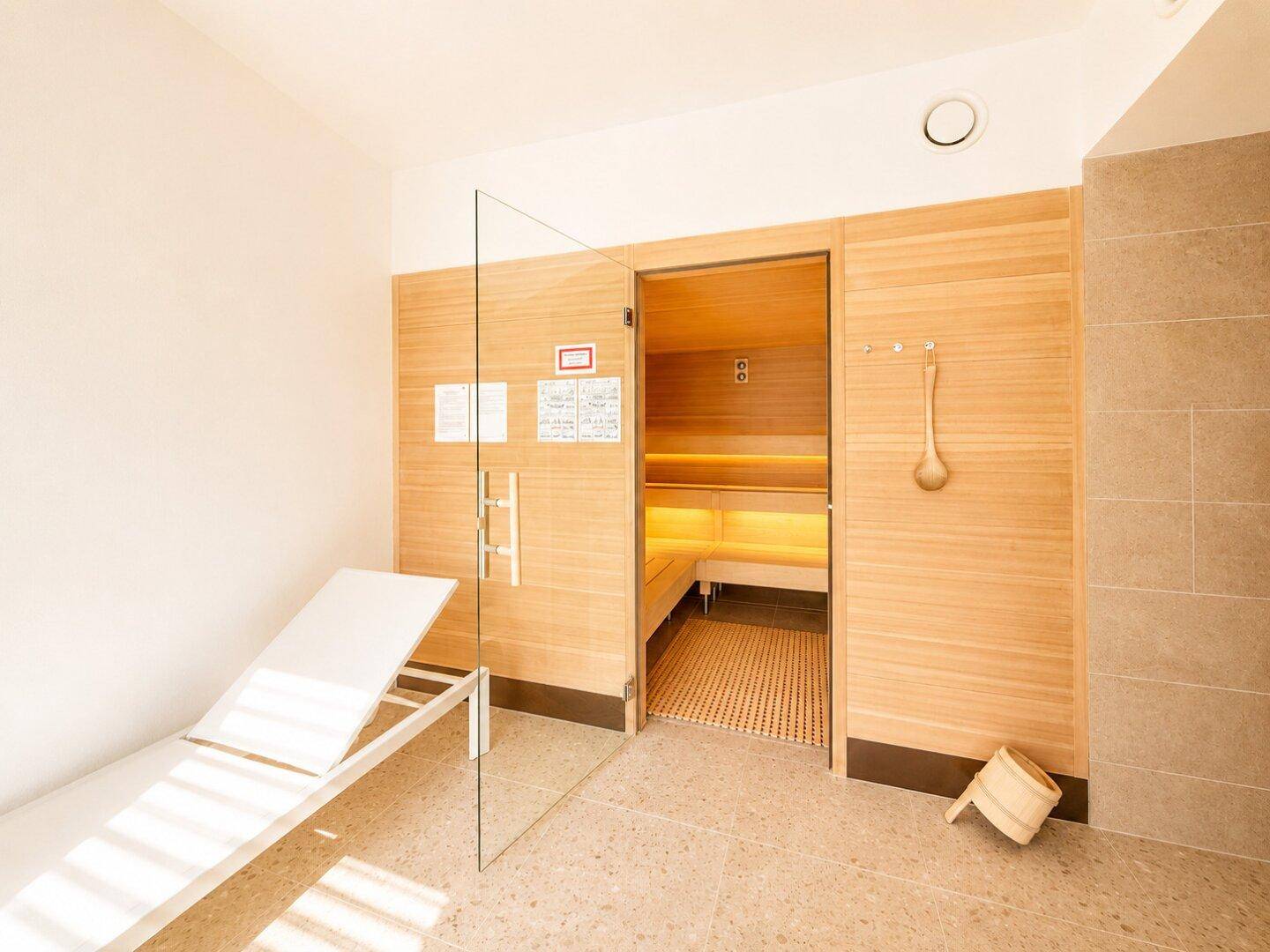 Entspannungsbereich mit Liege und Zugang zur Sauna, ausgestattet mit Holz und Glas.