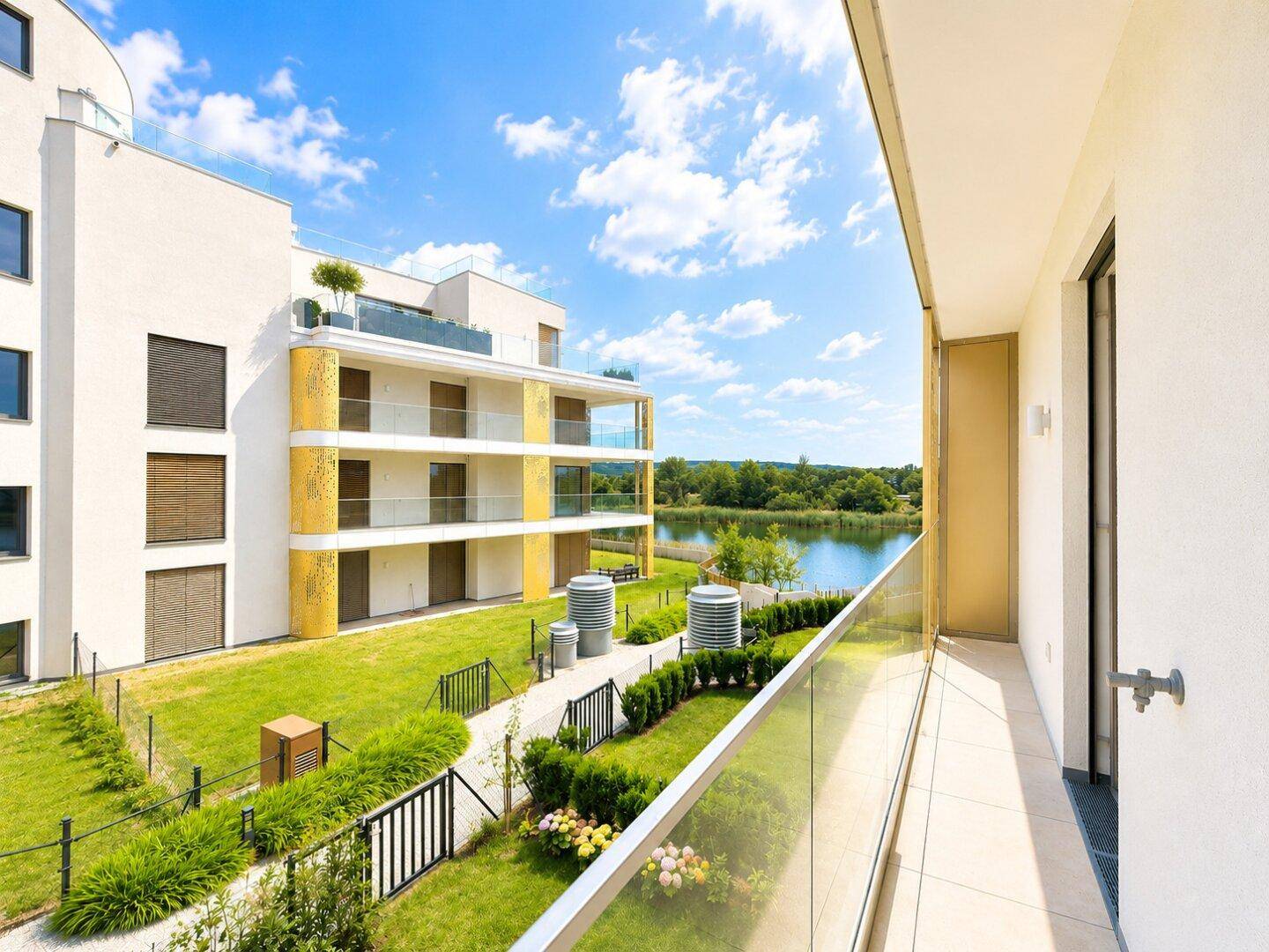 Blick vom Balkon auf die moderne Wohnanlage, den grünen Garten und den angrenzenden See.
