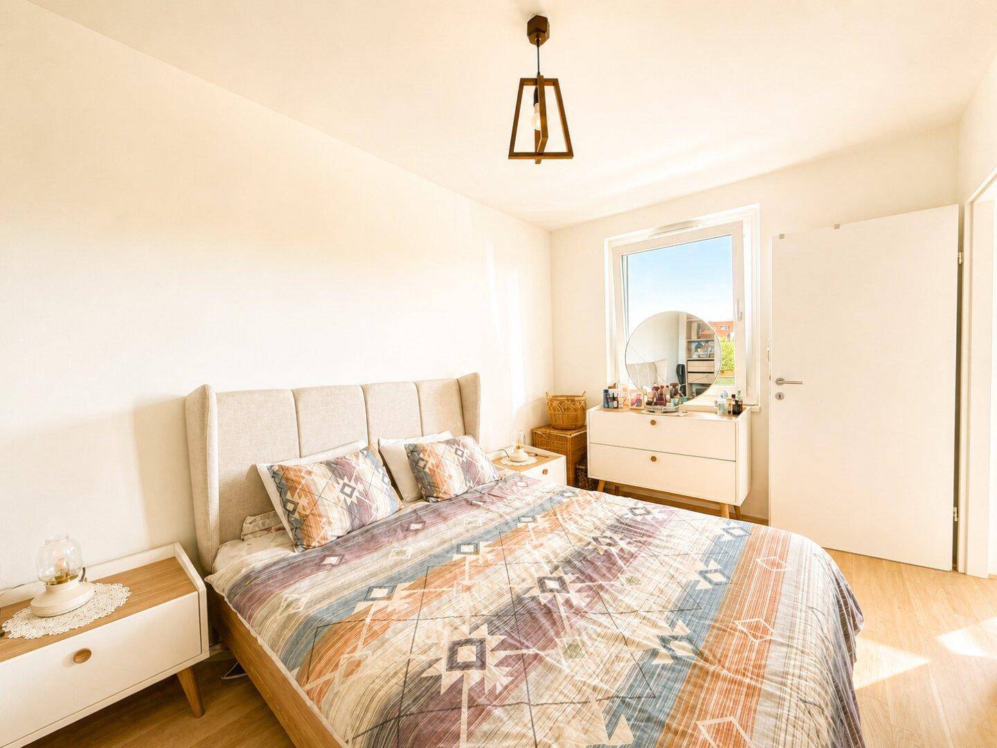 Helles Schlafzimmer mit Holzboden, bequemen Bett und einem Fenster mit Tageslicht.