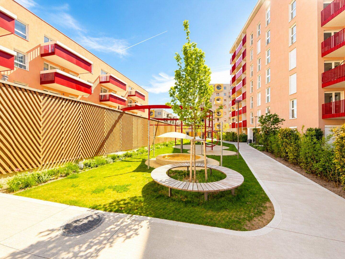Gepflegter Gemeinschaftsgarten mit Spielplatz, Sitzgelegenheiten und modernen Wohngebäuden im Hintergrund.