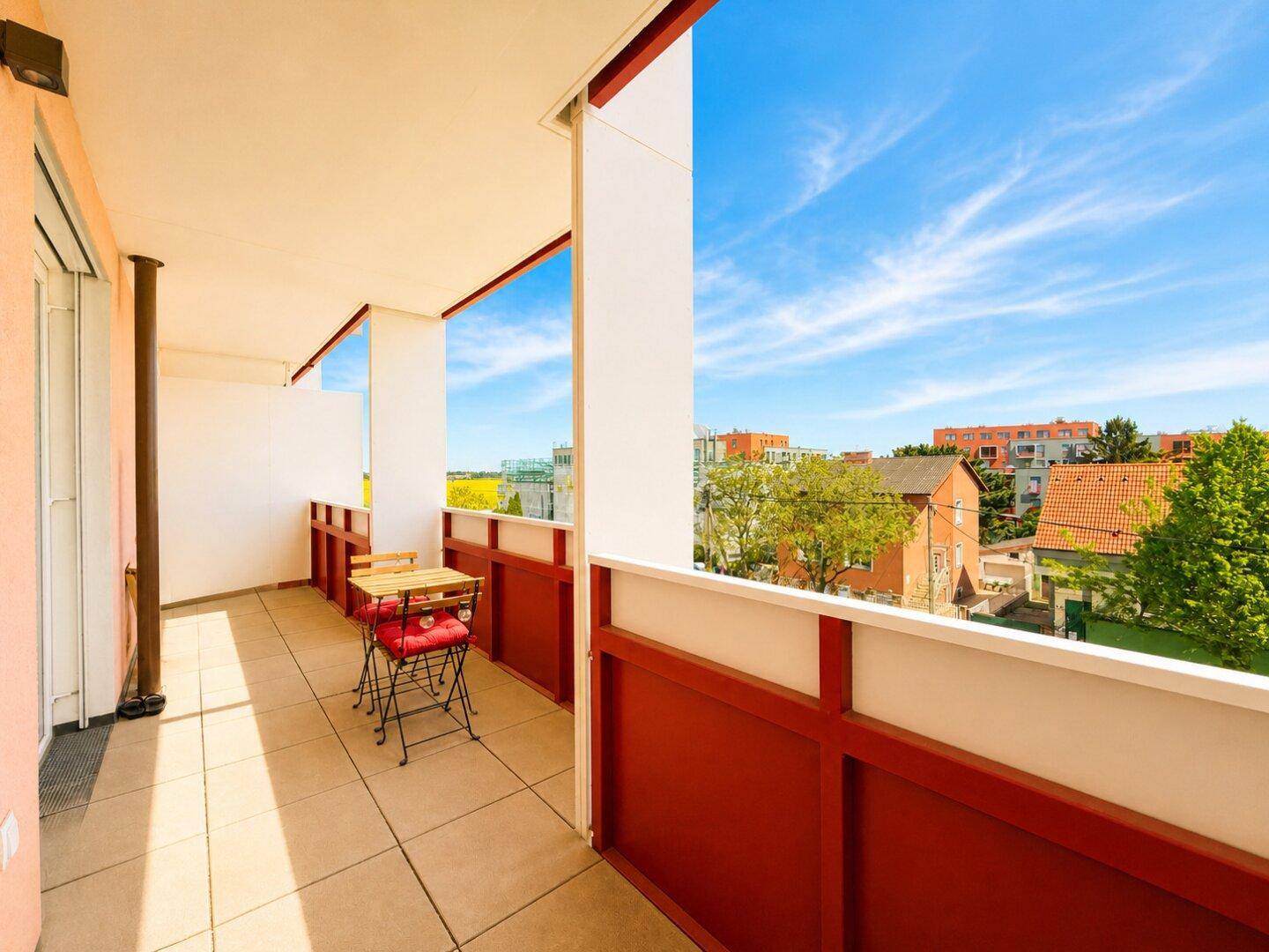 Geräumiger Balkon mit Fliesenboden und roter Brüstung, bietet einen weiten Blick über die Stadt.