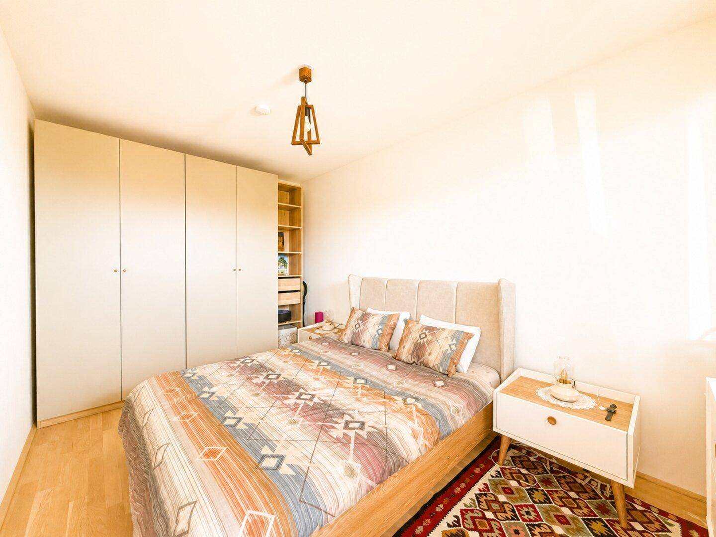 Schlafzimmer mit Holzboden, Einbauschränken und einem großen Bett mit gemusterter Decke.