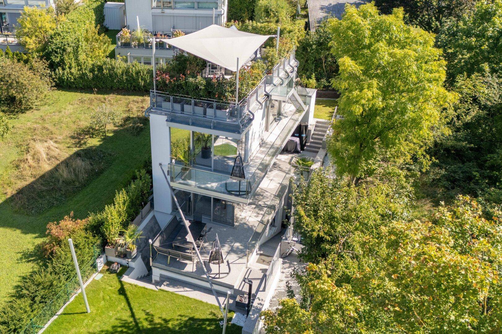 Ansicht der modernen Villa von oben mit gestuften Terrassen, Glasgeländern und umgebender Natur.