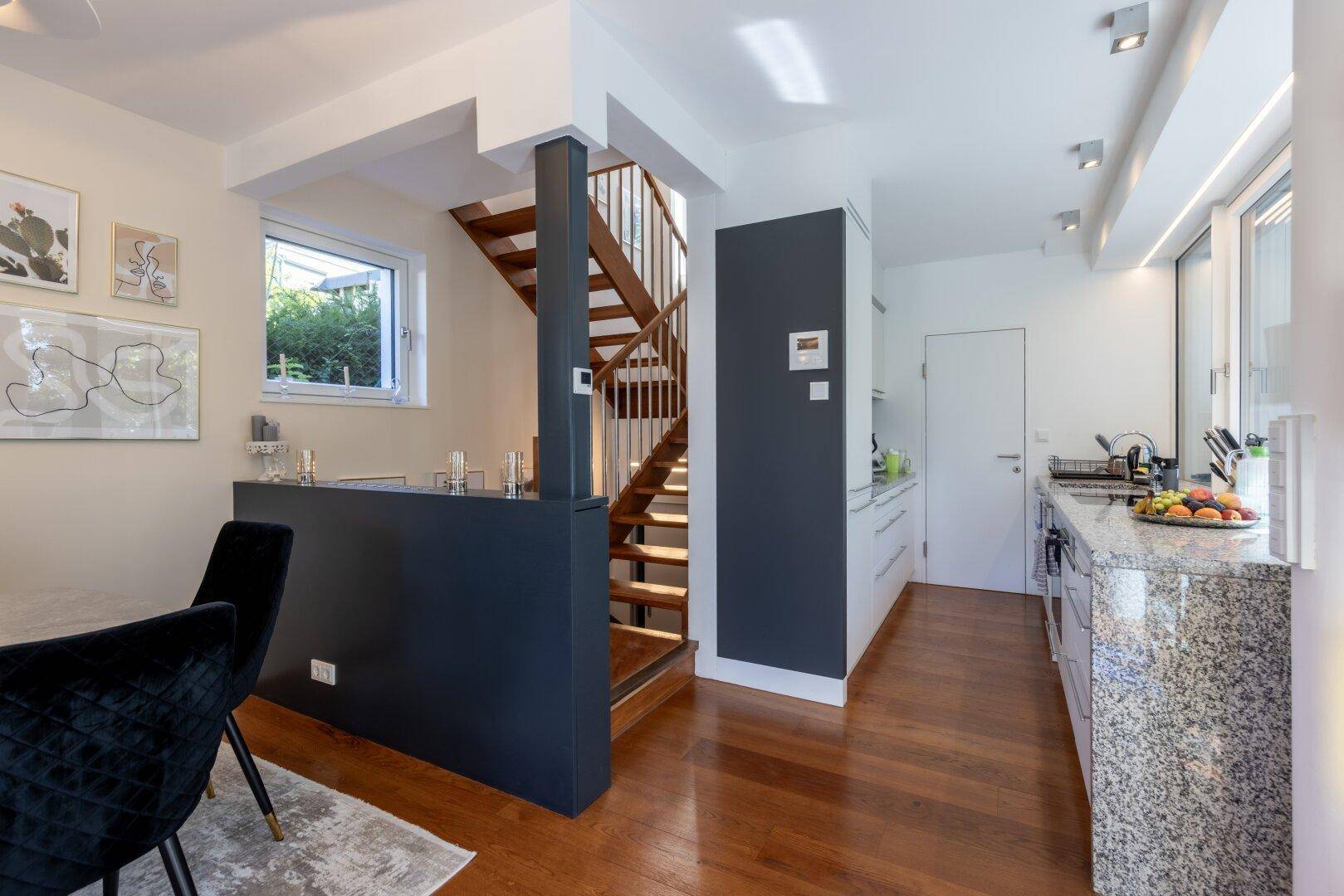 Moderne Küche mit Granitarbeitsplatte und Essbereich, verbunden durch eine elegante Holztreppe.
