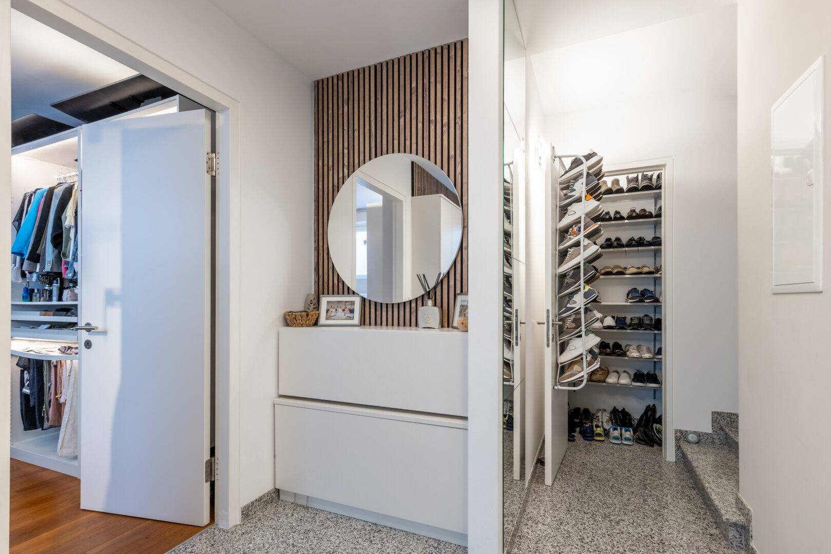 Heller Eingangsbereich mit modernem Schuhschrank, Spiegel und Zugang zu einem begehbaren Kleiderschrank.