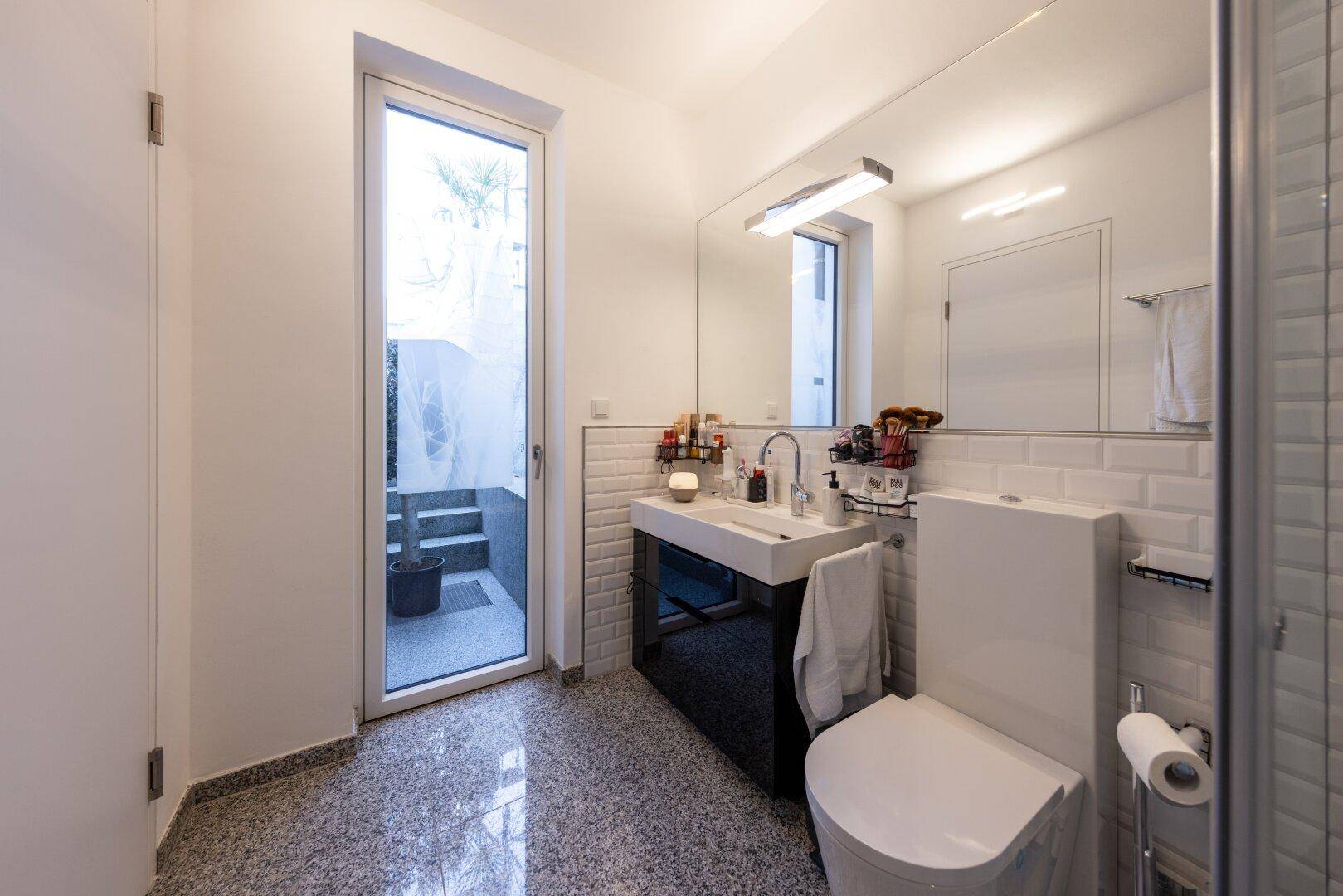 Modernes Badezimmer mit WC, Waschbecken und direktem Zugang zu einem kleinen Außenbereich.